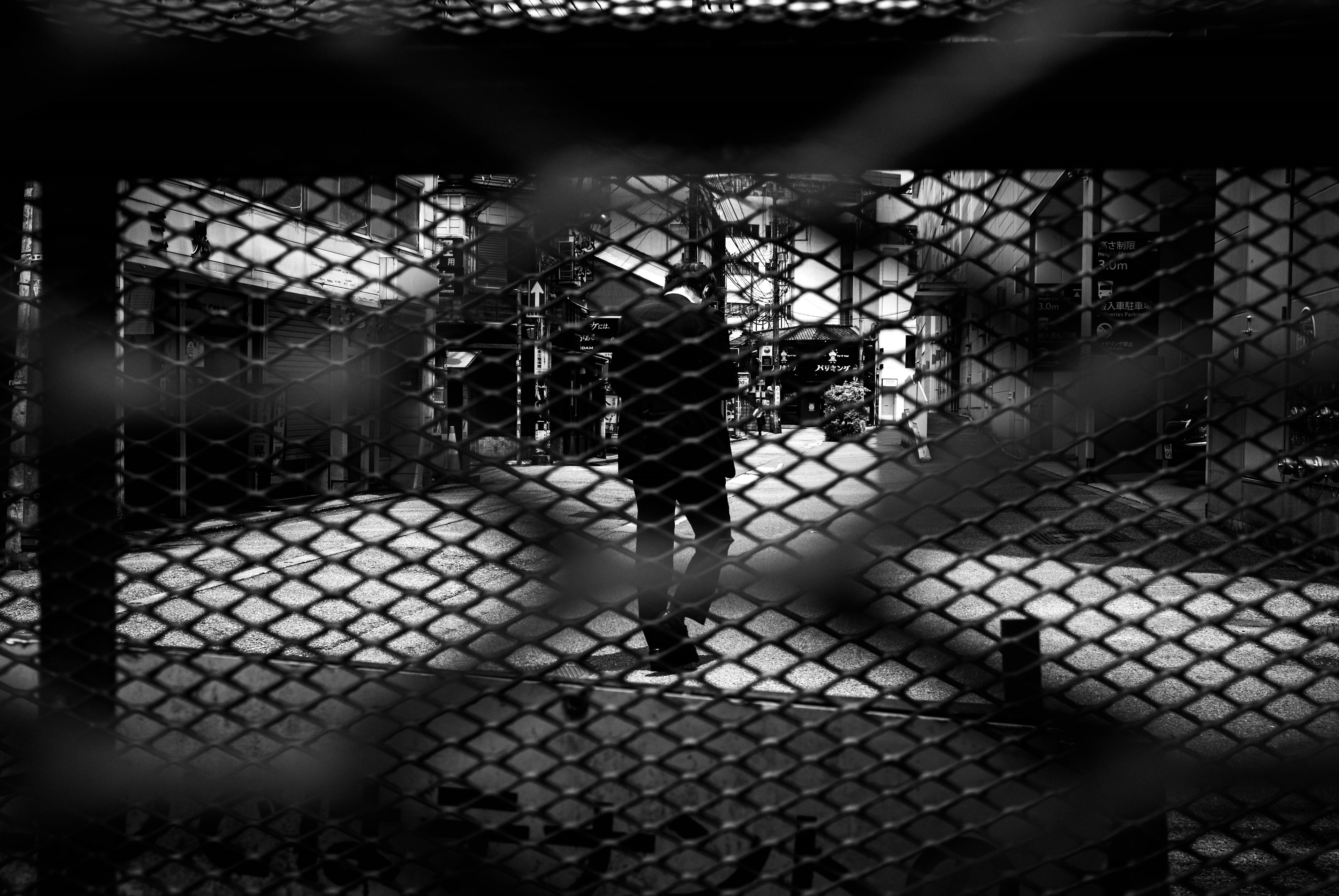 Person standing behind a mesh fence with blurred background structures