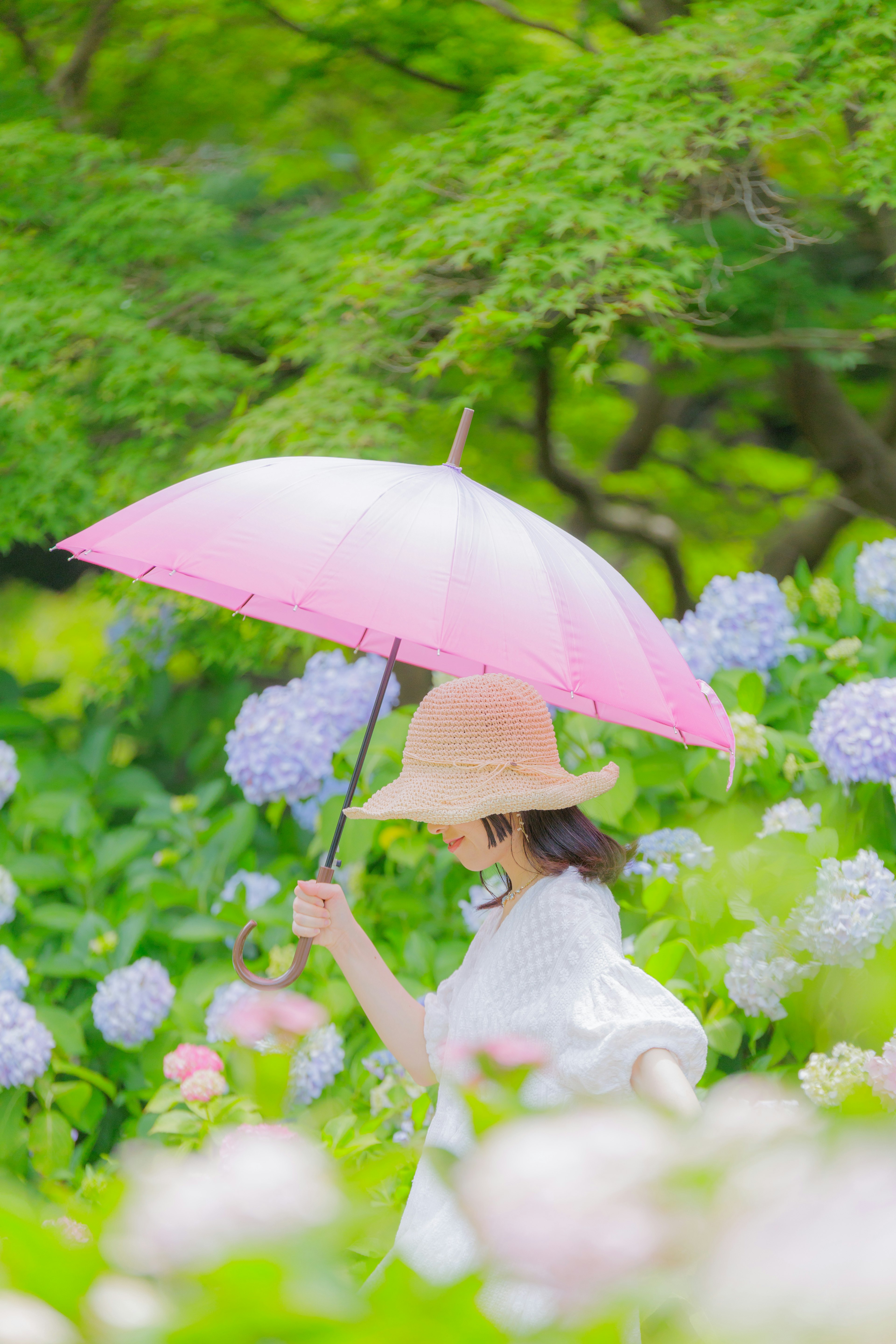 一位女性在花园中手持粉红色伞走动，周围是花朵