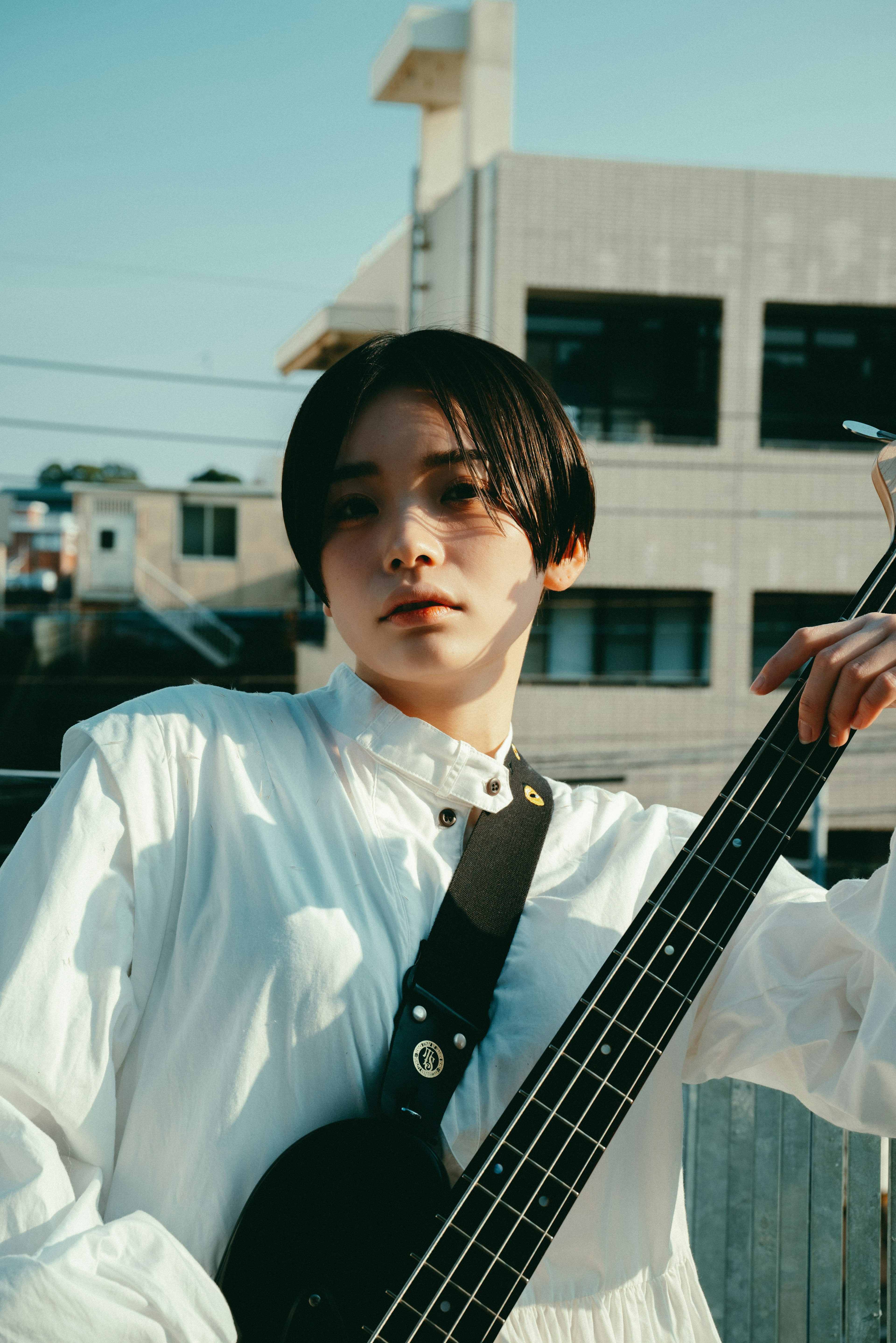 Joven músico con camisa blanca sosteniendo una guitarra baja negra