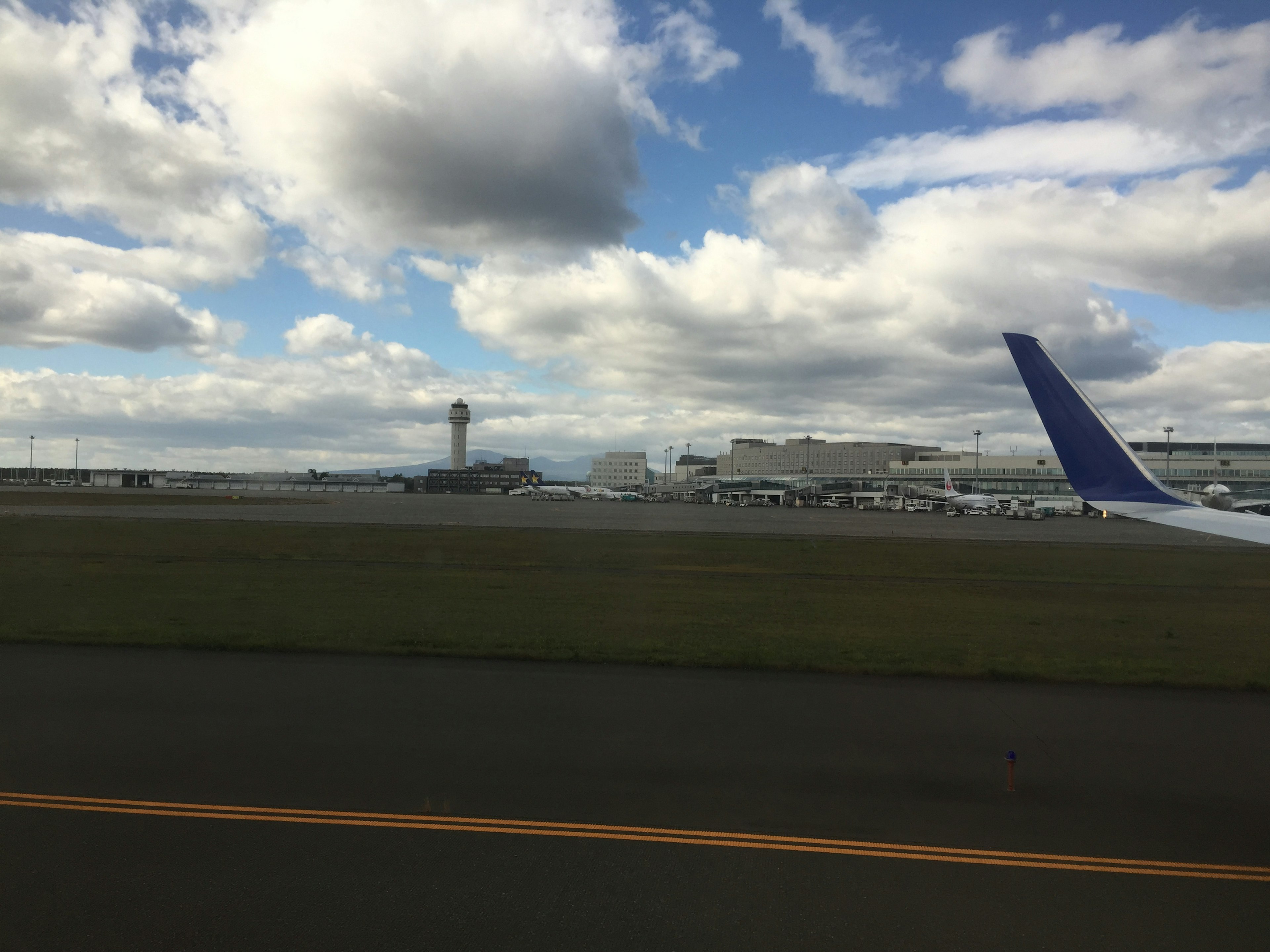 Ala de avión junto a la pista del aeropuerto con cielo azul y nubes