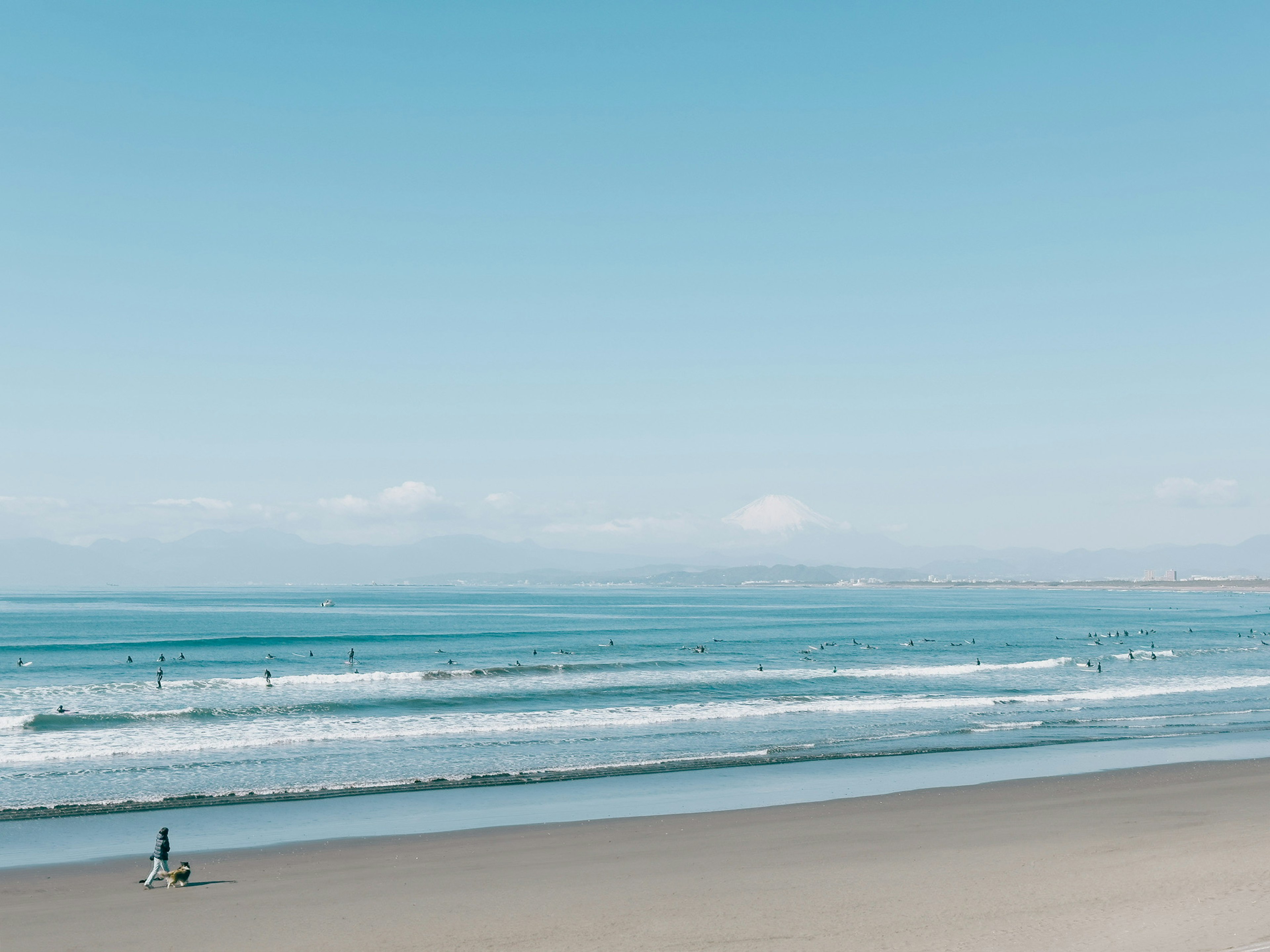 Una persona che cammina su una spiaggia con onde dolci e un cielo blu chiaro