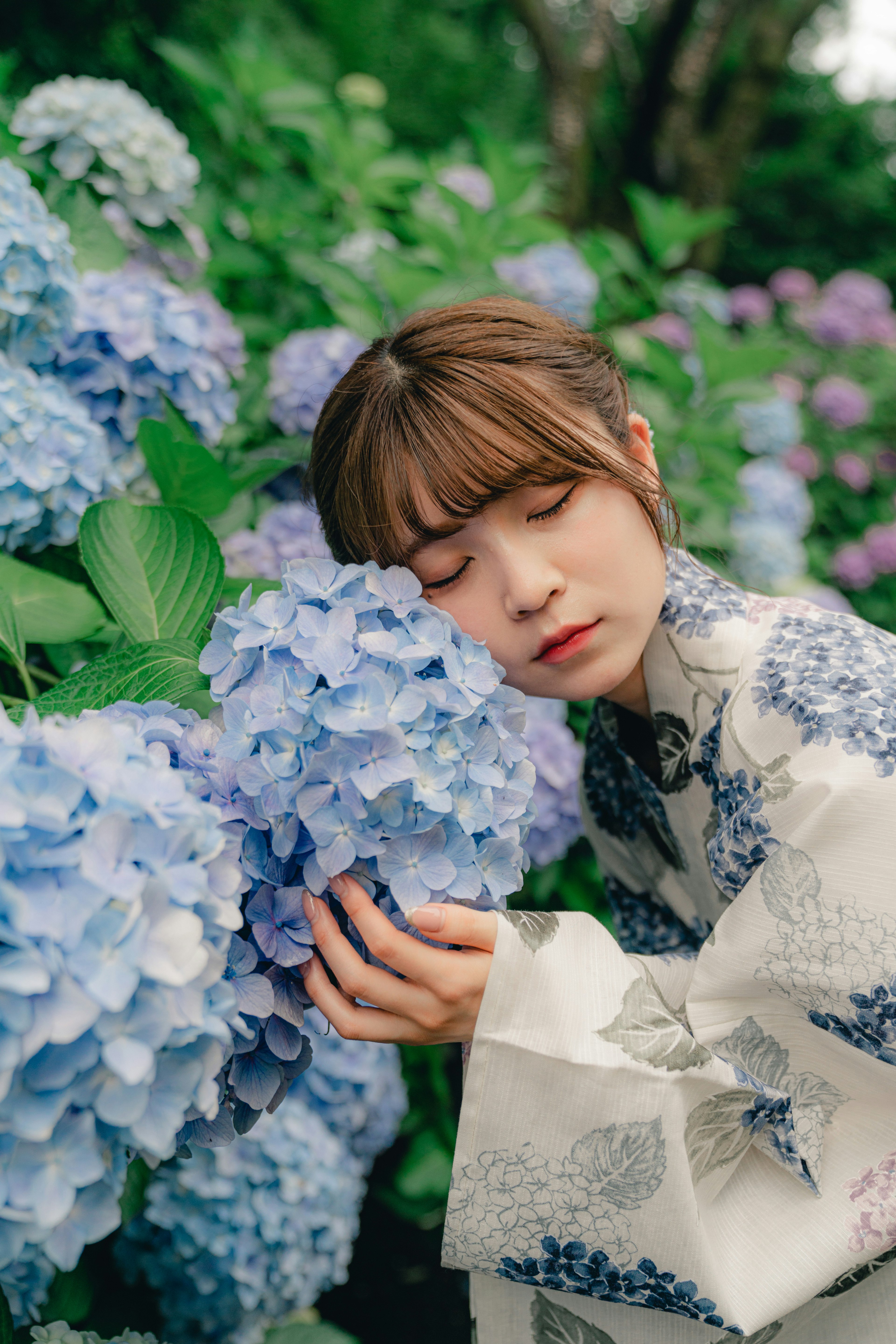 Frau umarmt blaue Hortensienblüten in einem Garten