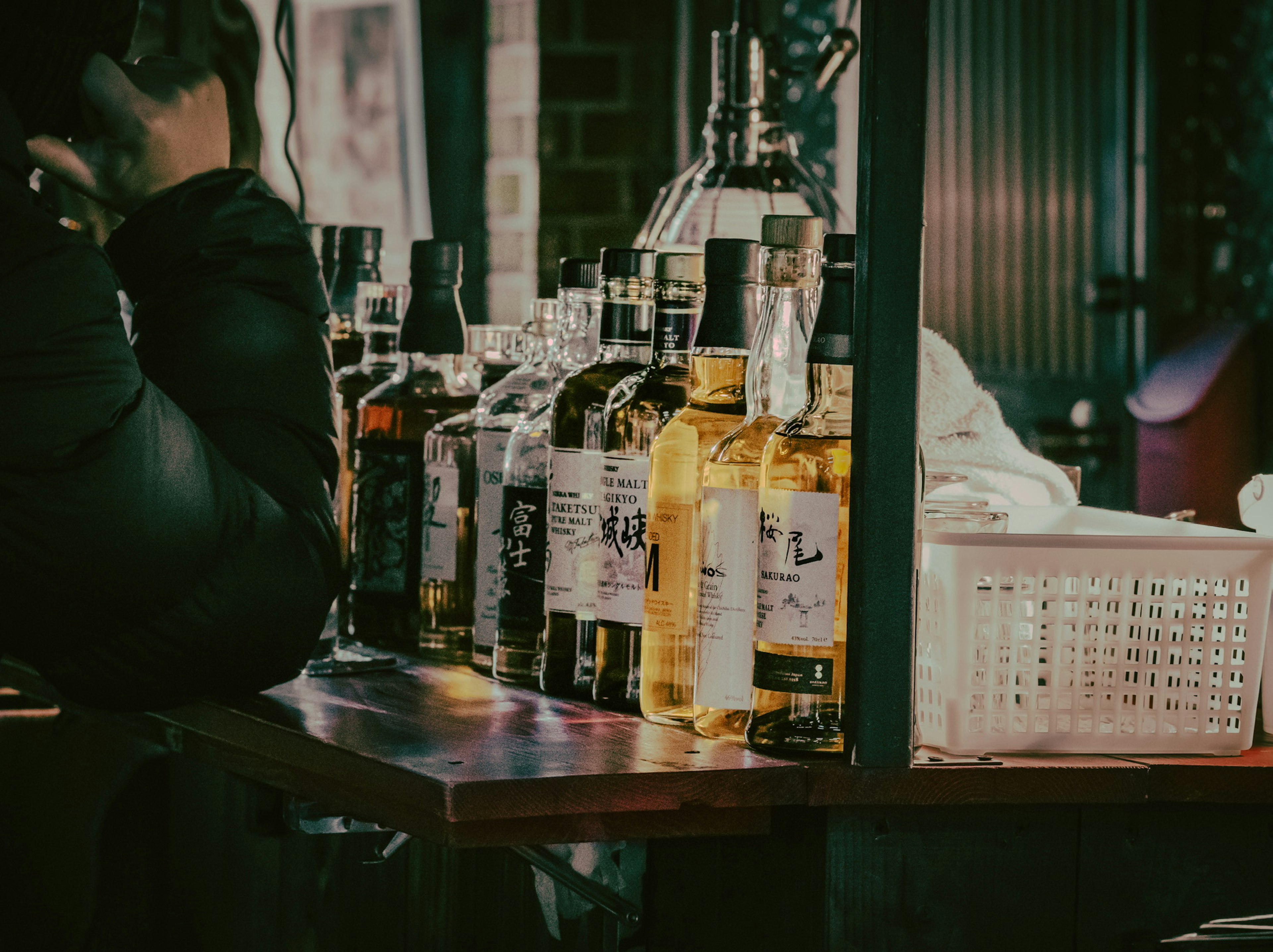 Varias botellas de whisky alineadas en un mostrador de bar con la mano de una persona