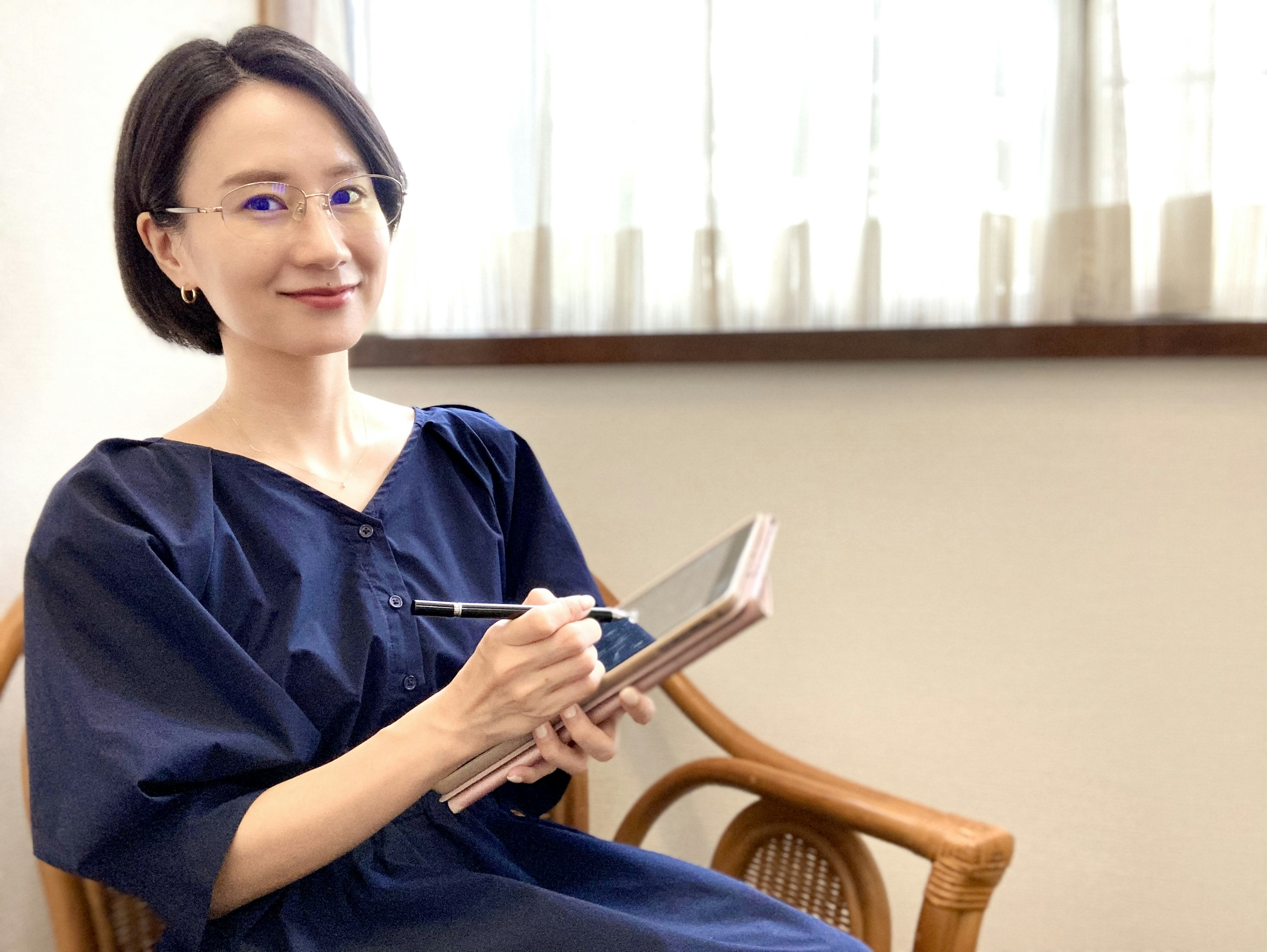 Frau in blauem Kleid sitzt auf einem Stuhl und schreibt in ein Notizbuch