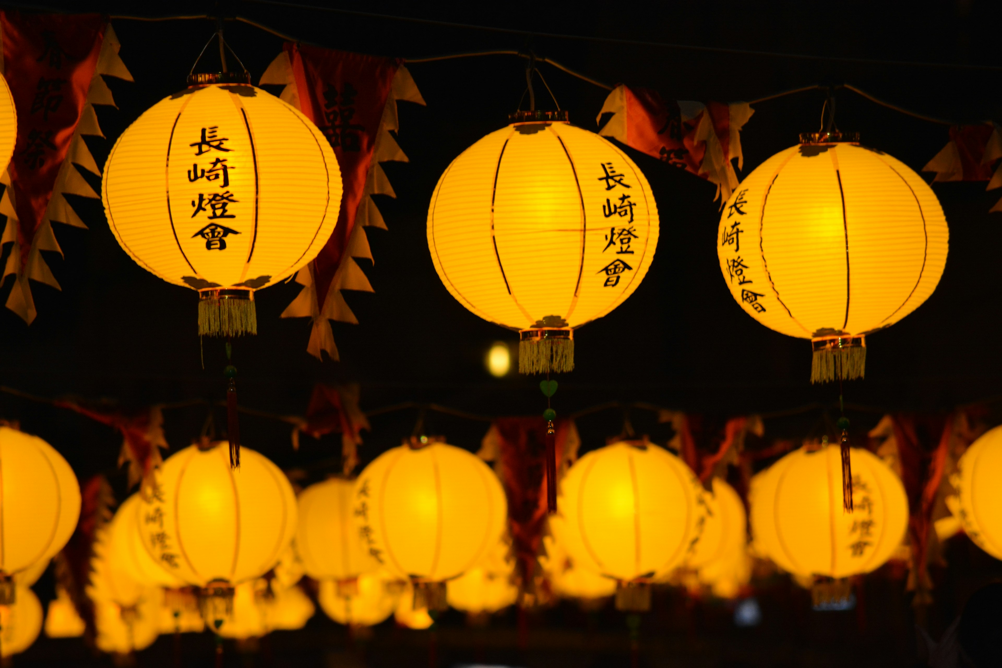 A row of illuminated yellow lanterns with Chinese characters hanging against a dark background