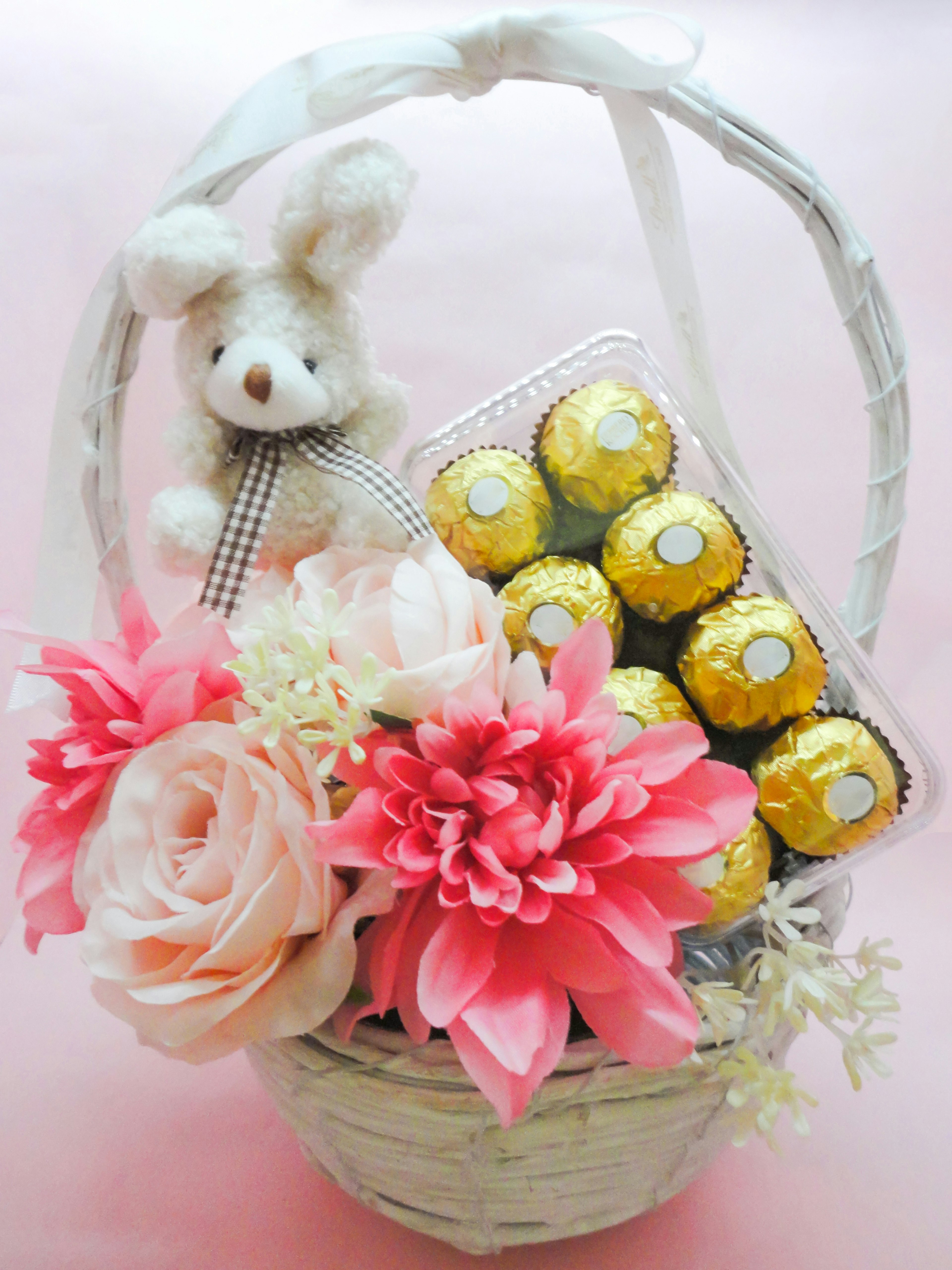 A cute basket filled with flowers and chocolates featuring a plush bunny