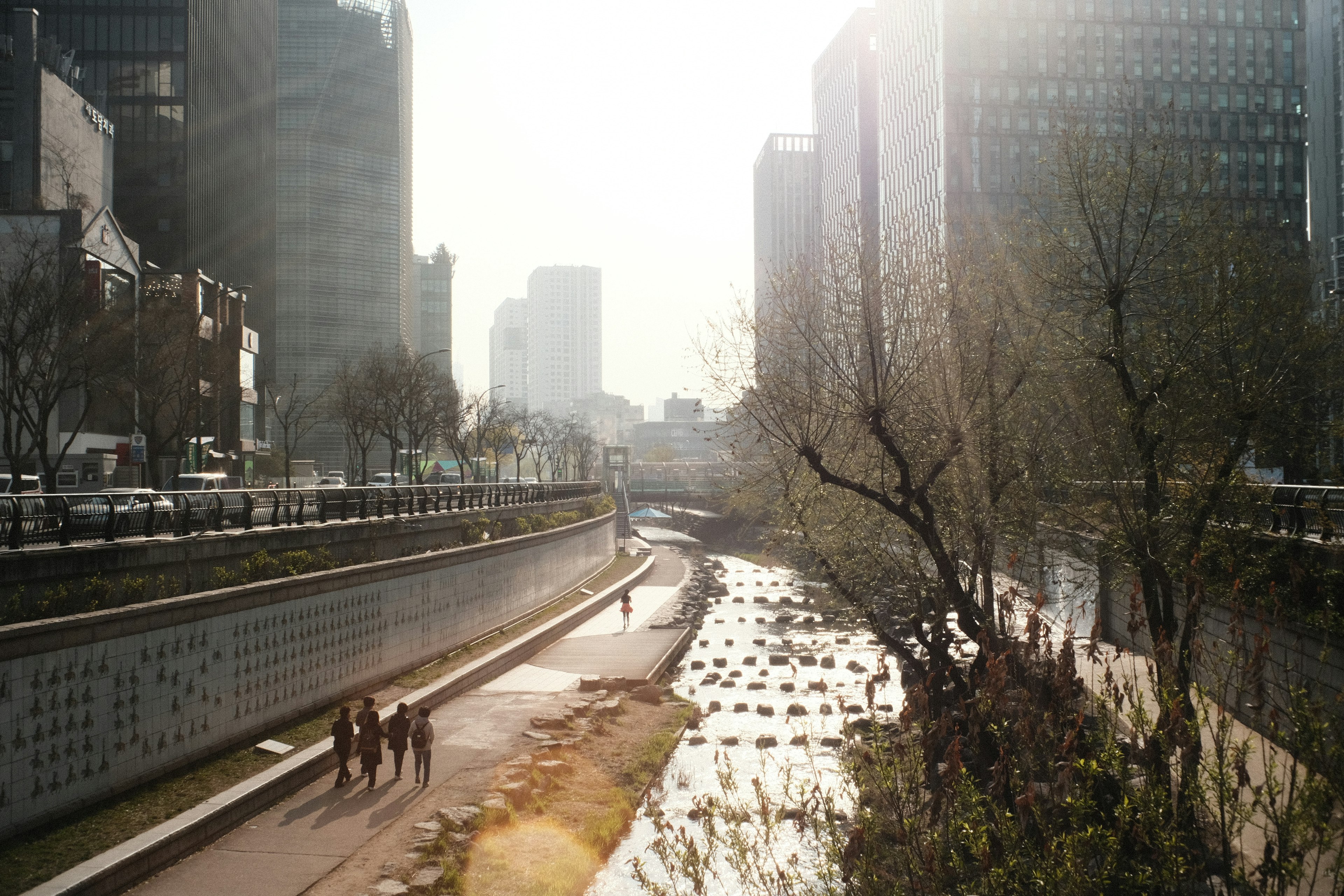 People walking along a river in an urban setting with skyscrapers