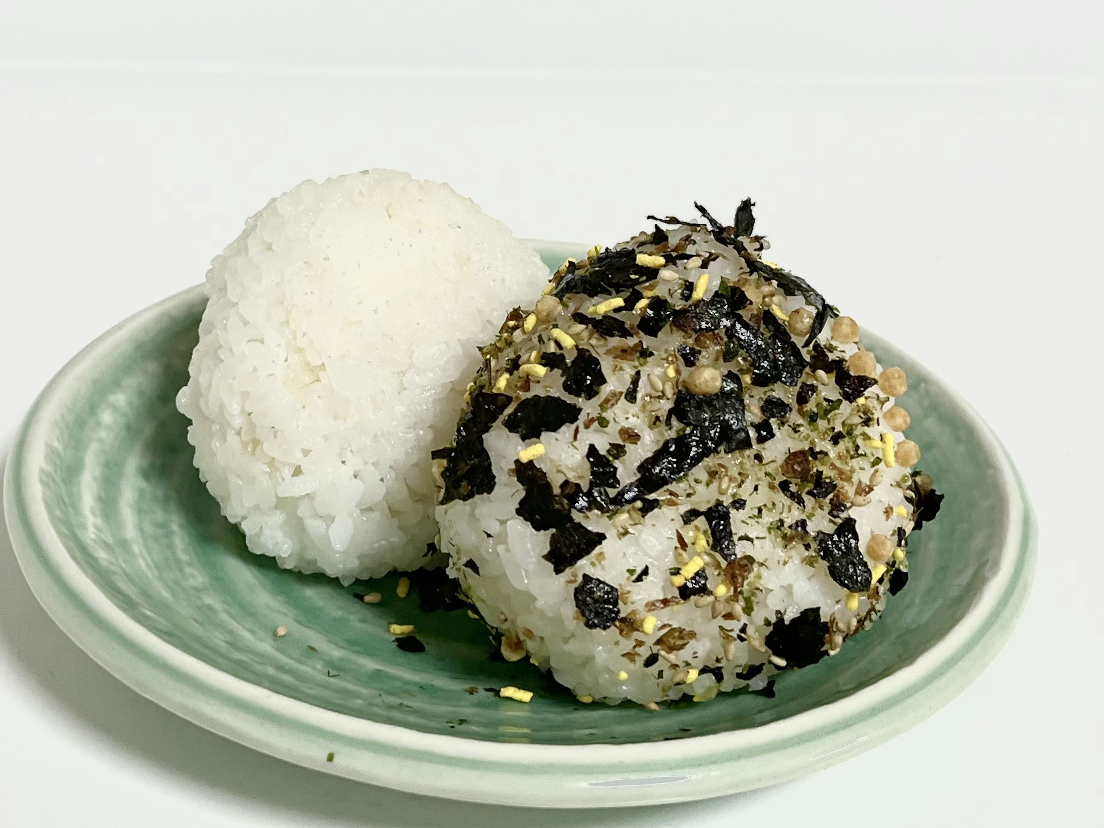 Dos bolas de arroz en un plato verde una simple y otra cubierta con alga y condimentos