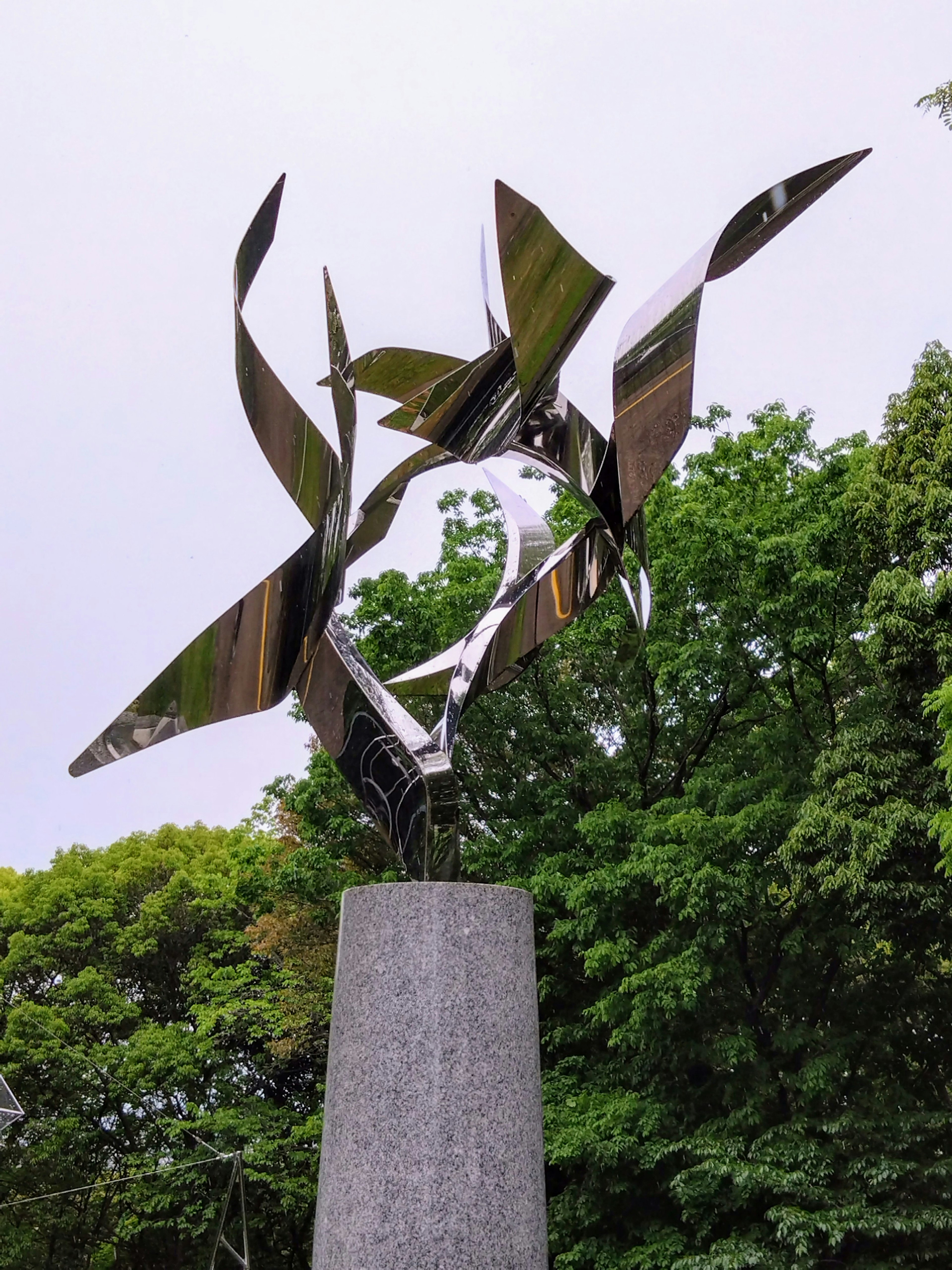 Abstract metal sculpture standing in front of green trees