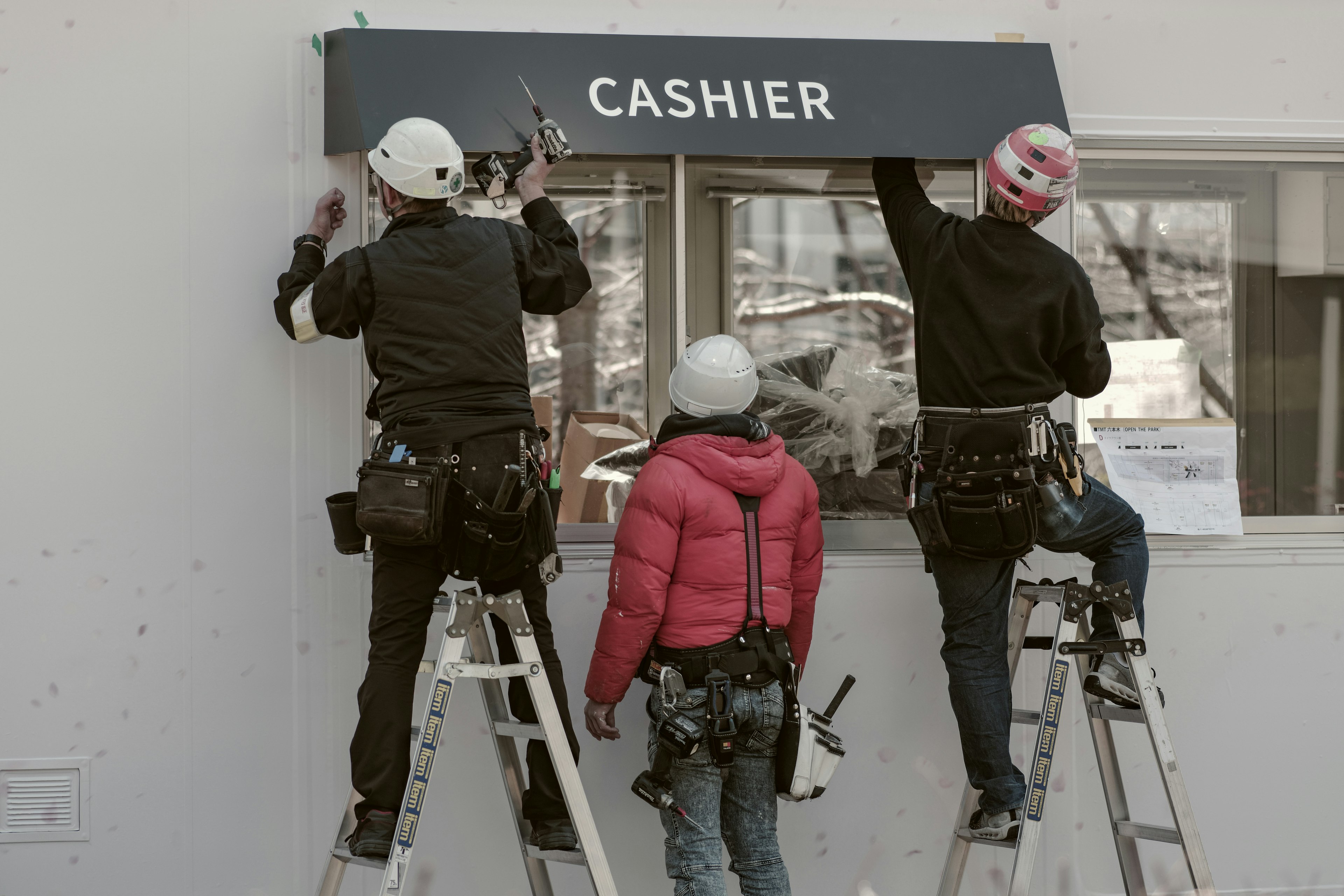 Workers installing a cashier sign using ladders