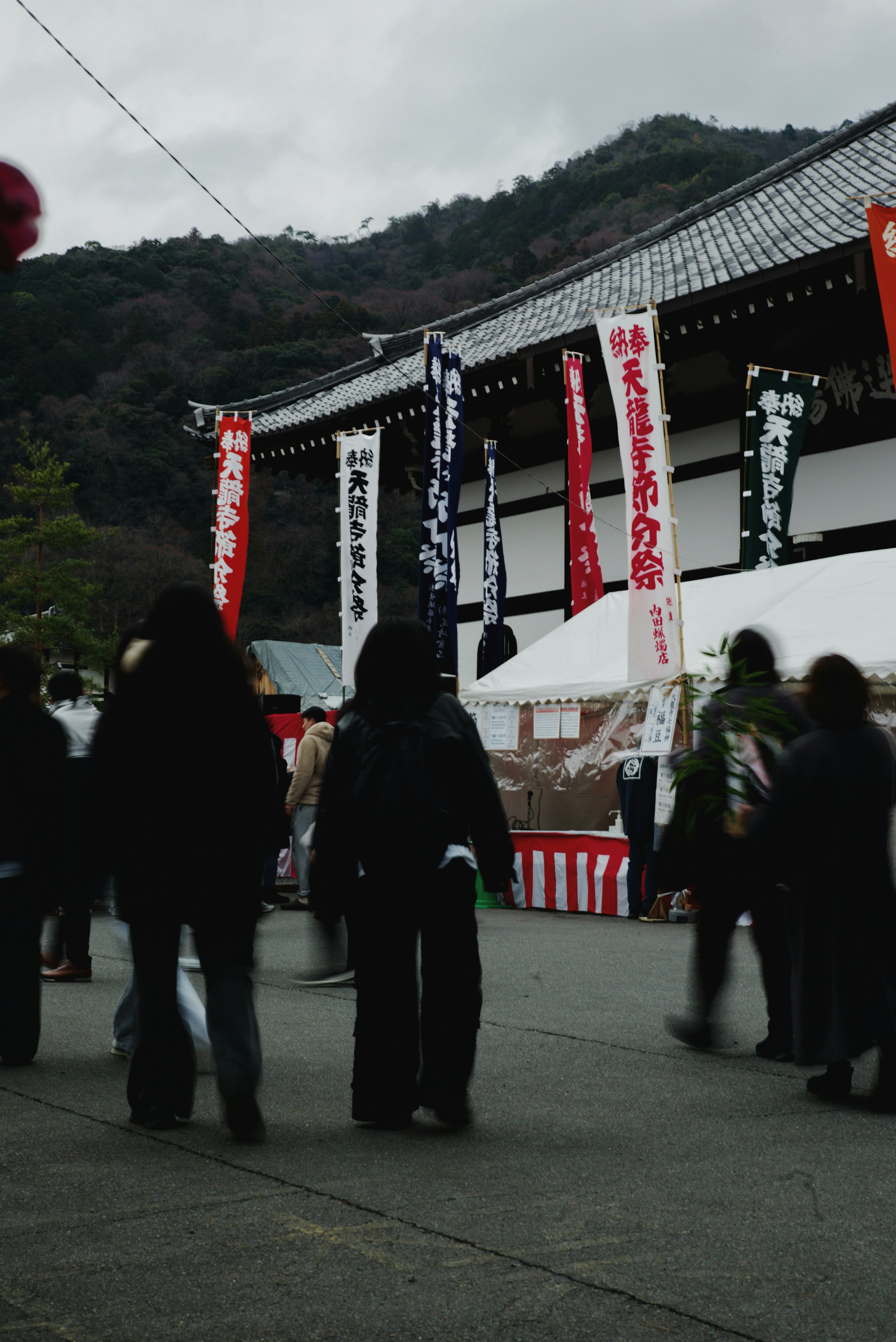 人々が山の背景の寺院の前を歩いている様子赤いと白い旗が掲げられている