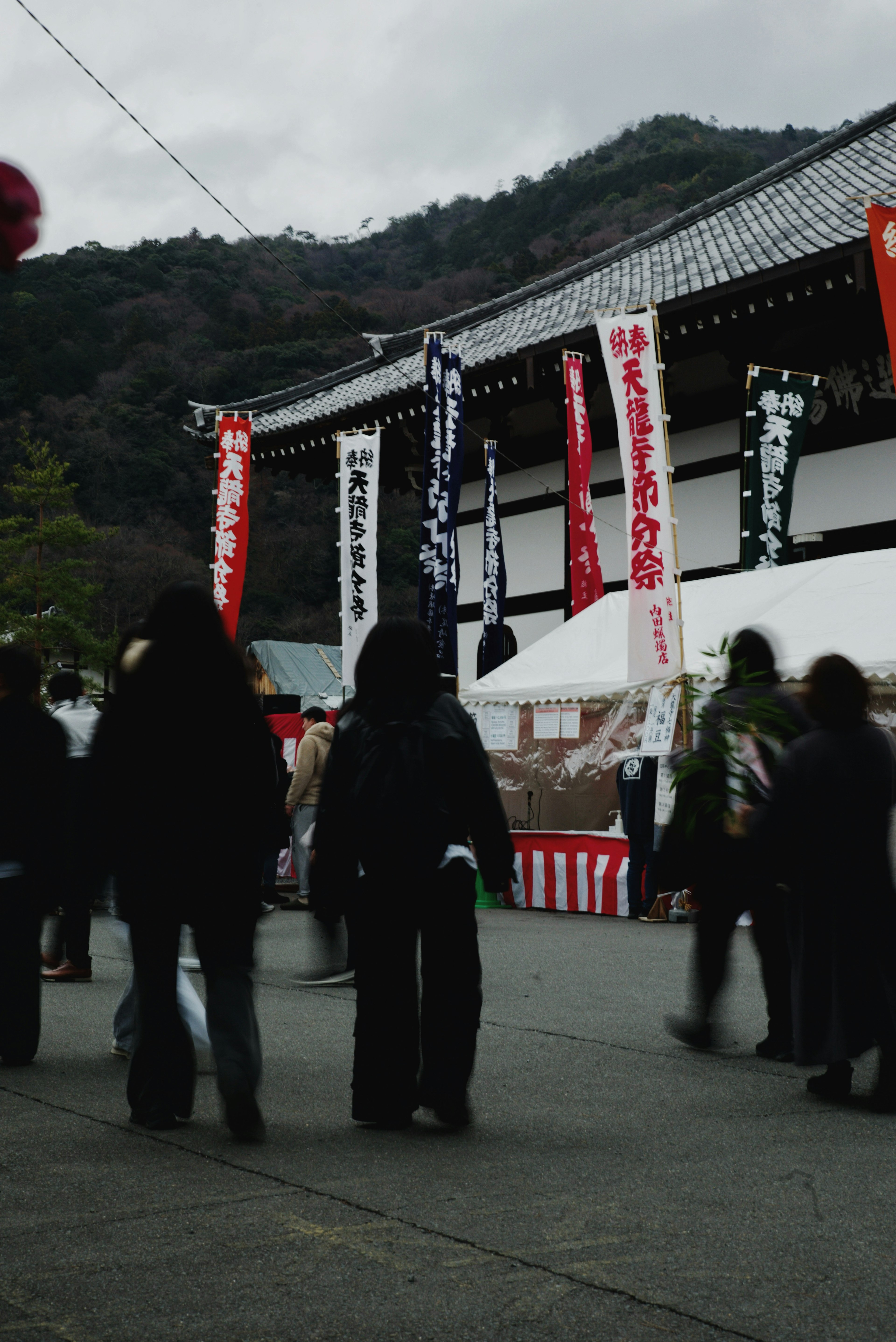 People walking in front of a temple with mountains in the background red and white banners displayed