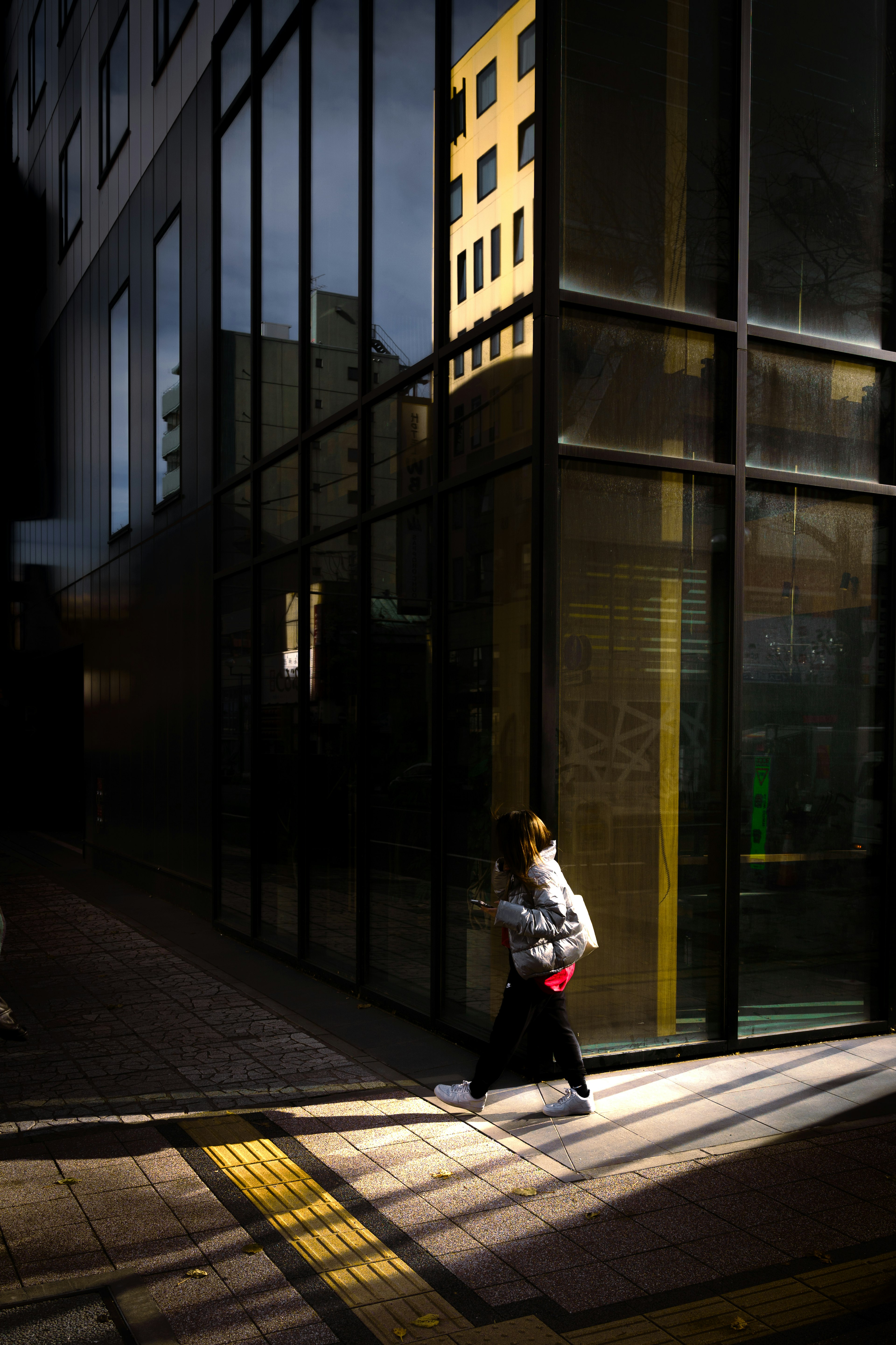 Silhouette of a woman walking in front of a glass building with contrasting shadows