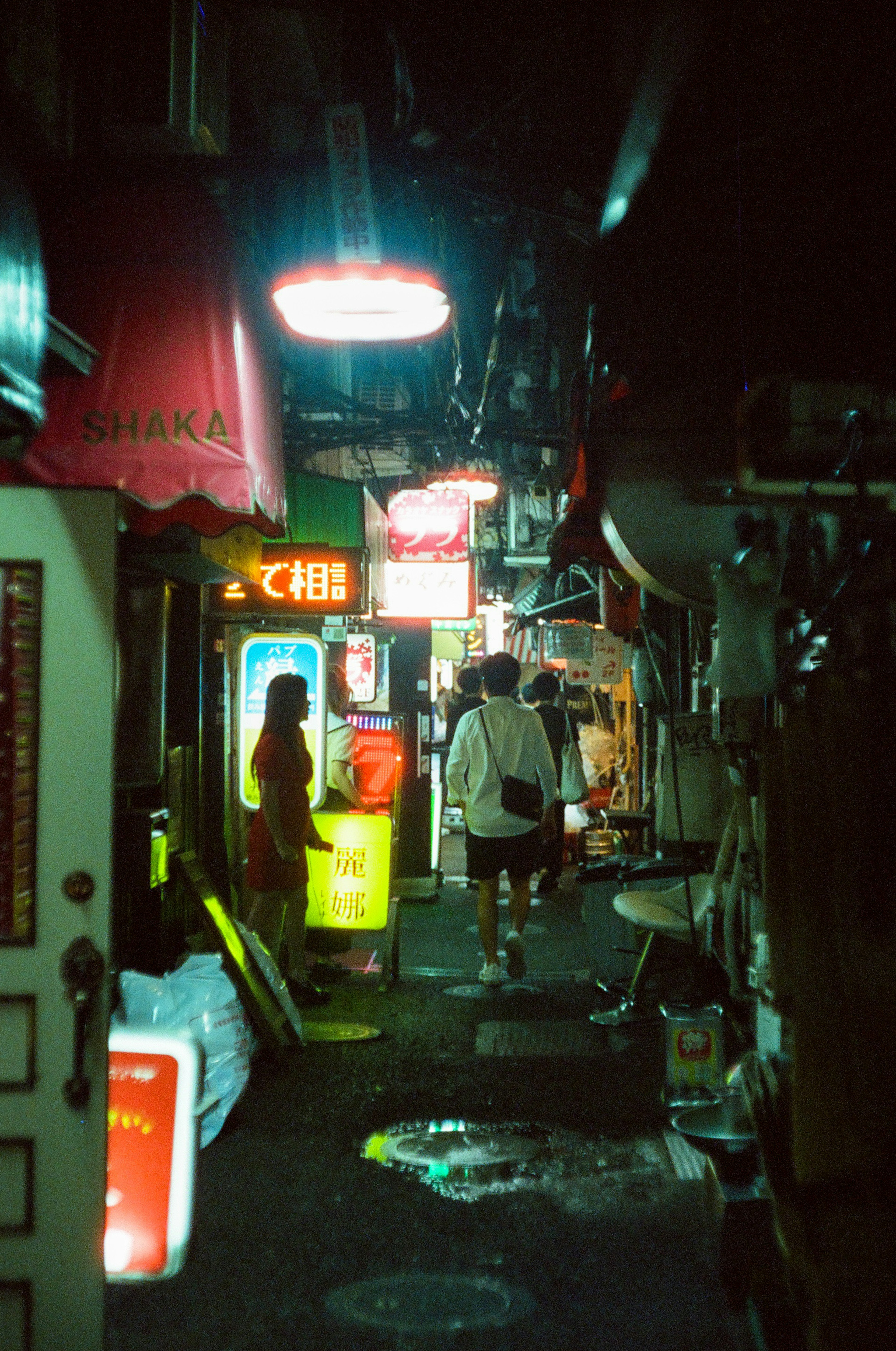 Callejón estrecho de noche con personas y letreros de neón