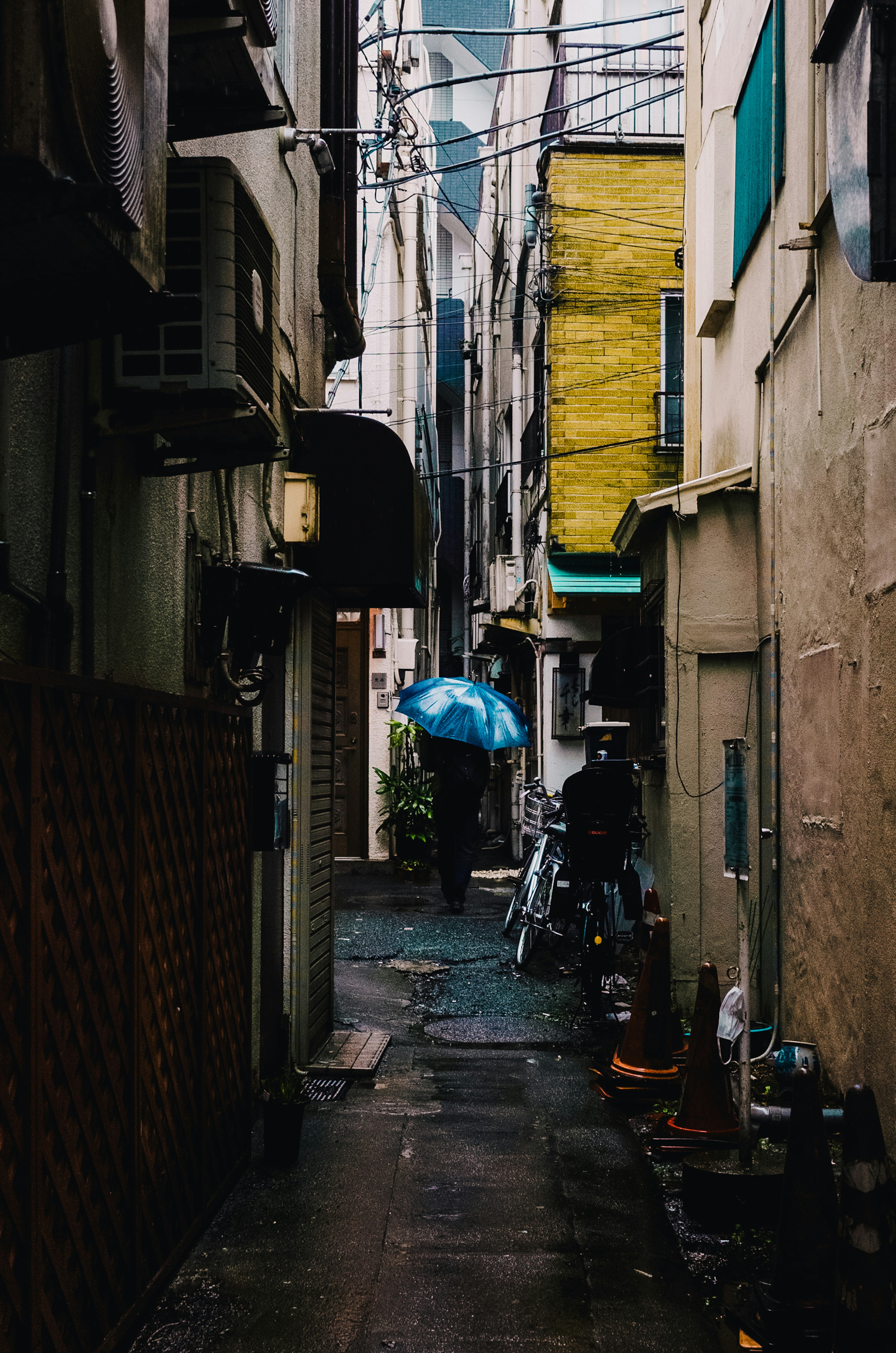 狭い路地に青い傘を持った人物がいる街の風景