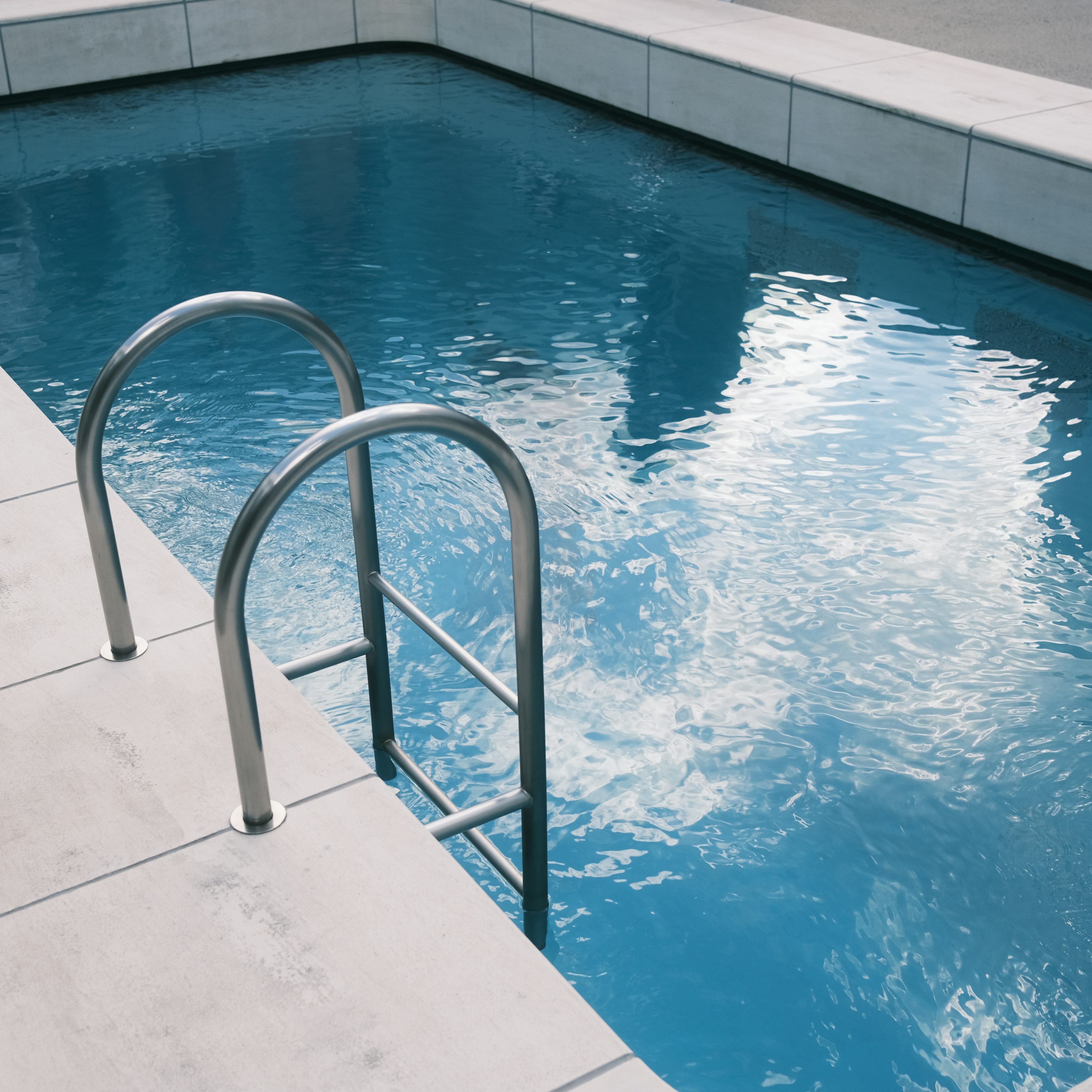 Una piscina con superficie azul y una escalera de metal