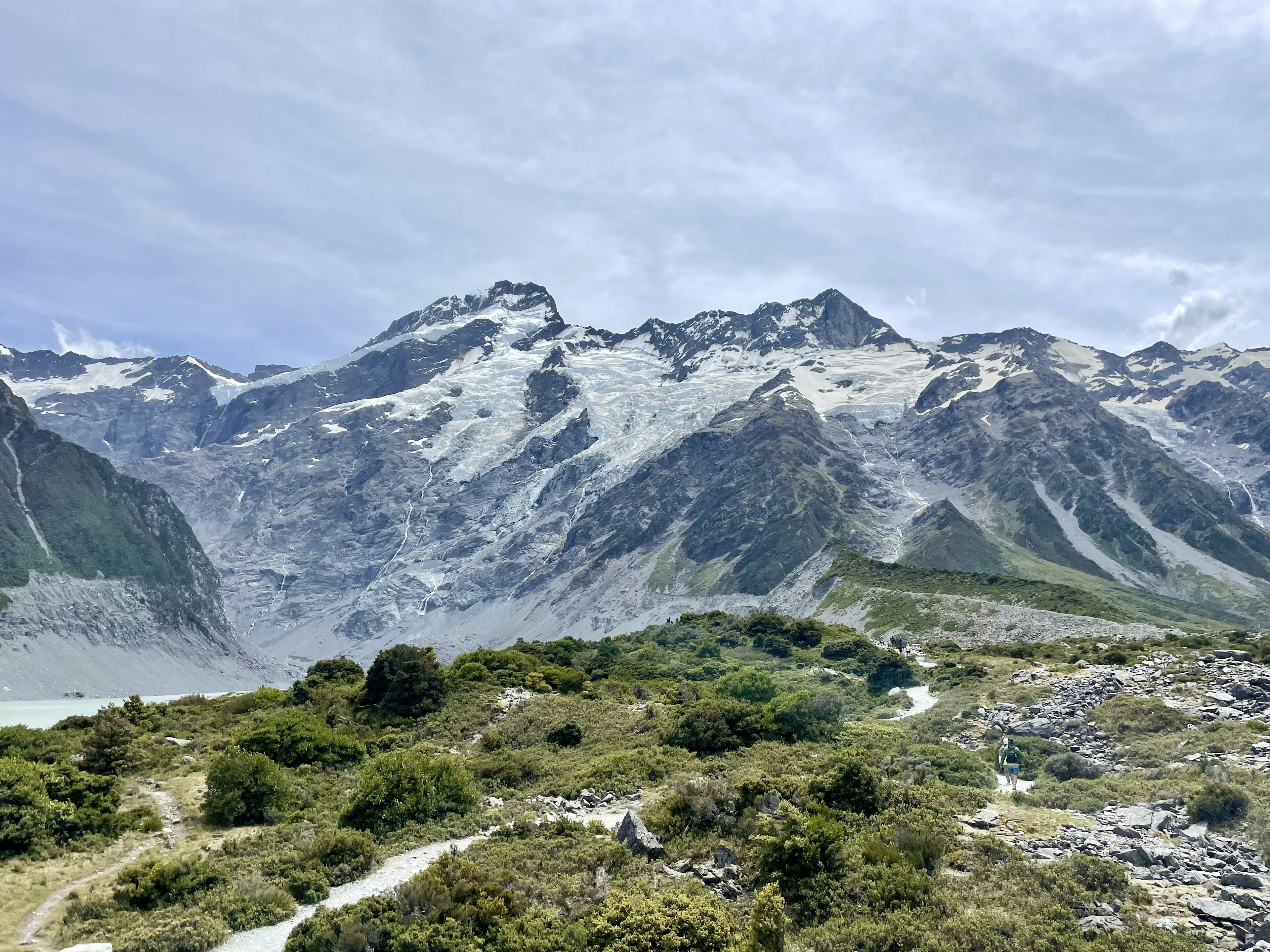 Landschaft mit schneebedeckten Bergen und grünen Hügeln unter einem bewölkten Himmel