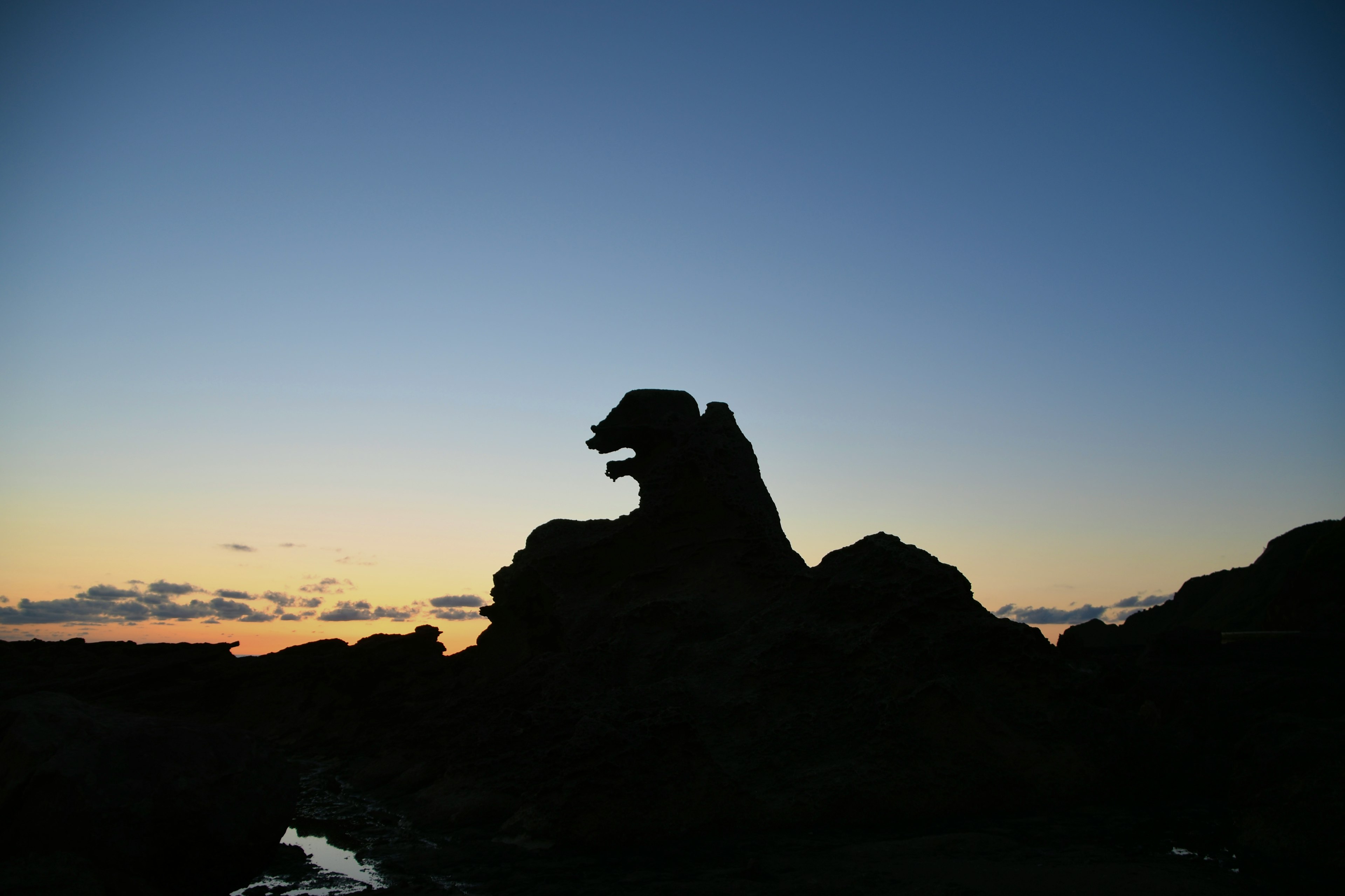 夕暮れの海岸にある岩のシルエットが獅子の形をしています