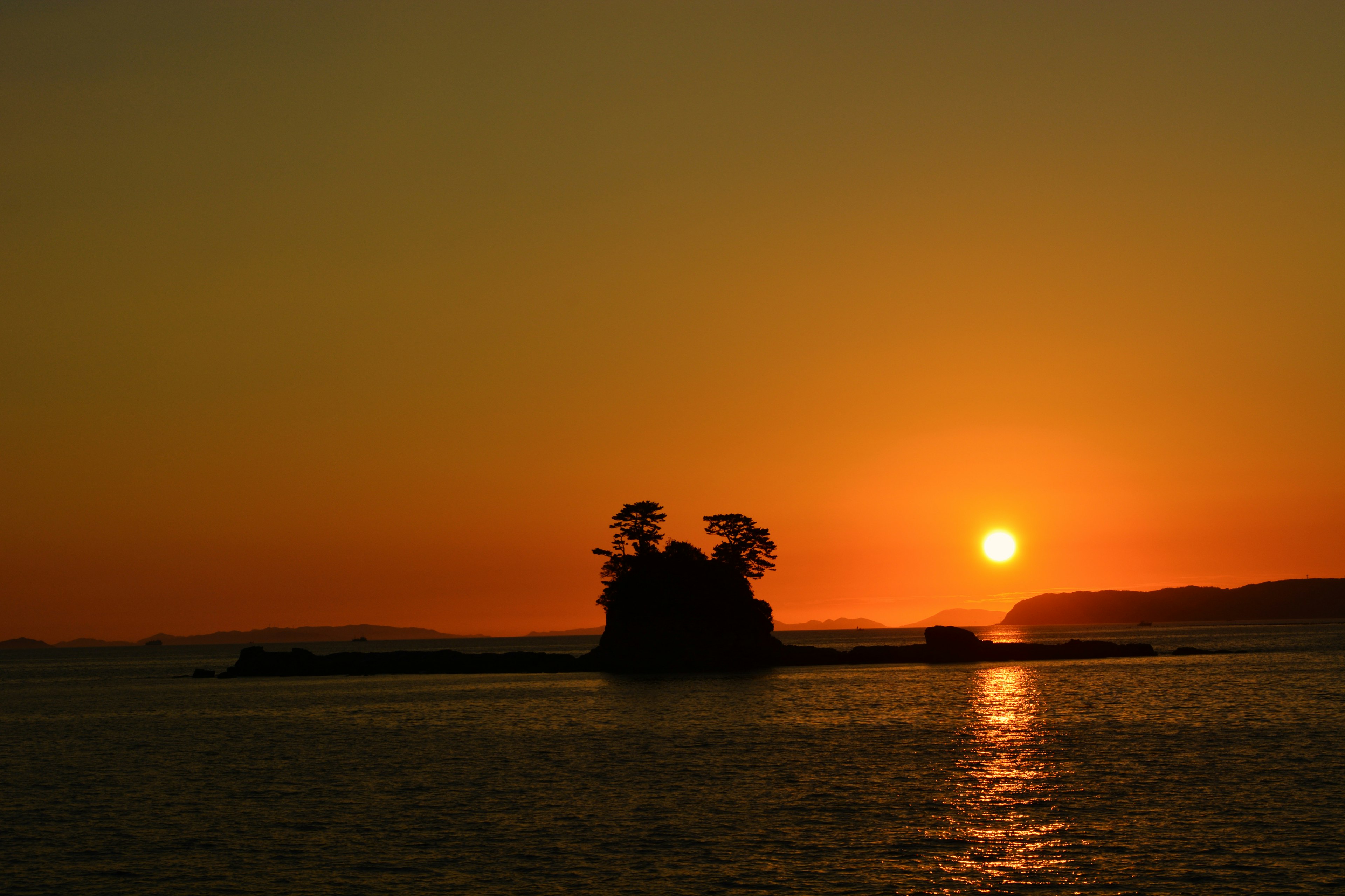 Silhouette of a small island against a sunset over the sea