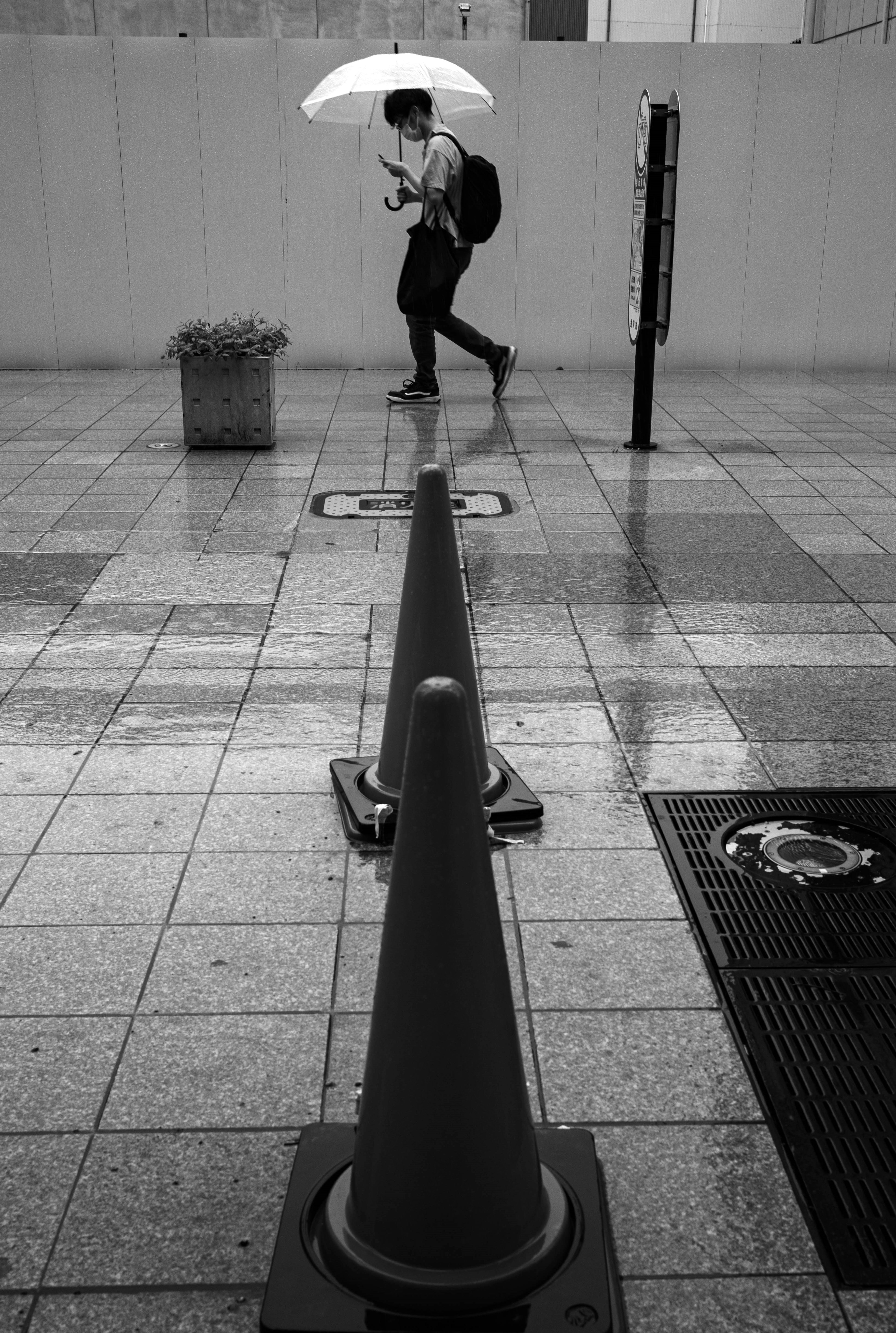 A person walking with an umbrella on a rainy day with traffic cones