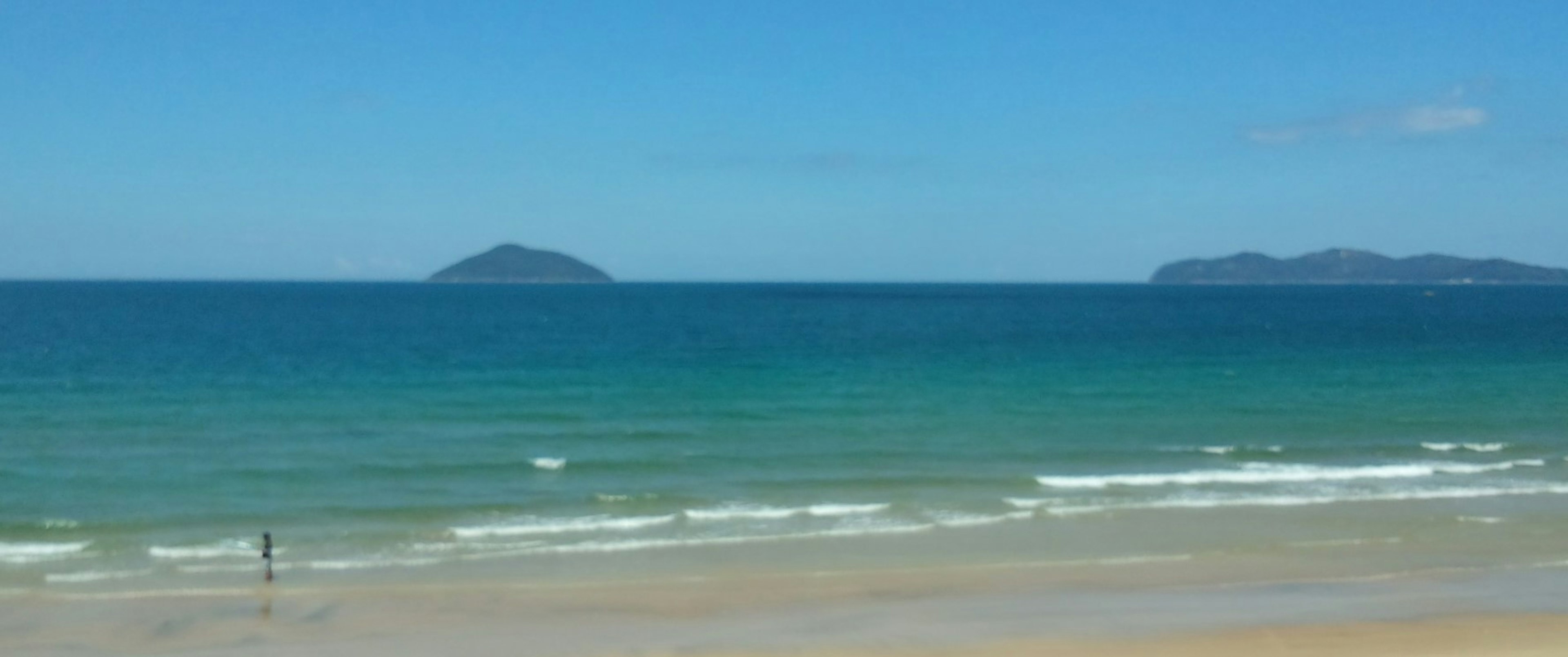 Una vista escénica del océano azul y el cielo con una persona caminando por la playa