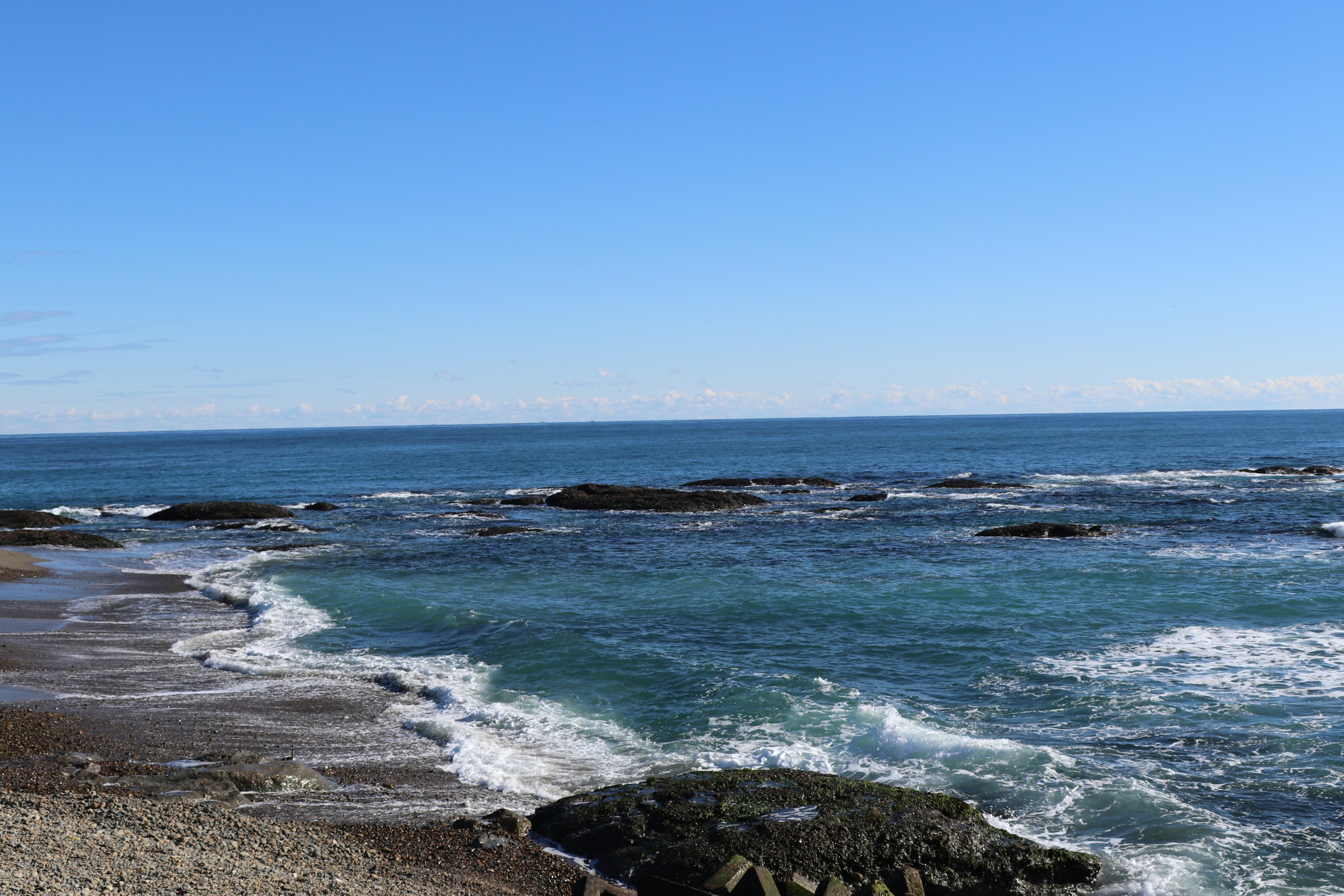 Scenic view of blue ocean and bright sky featuring rocks and waves