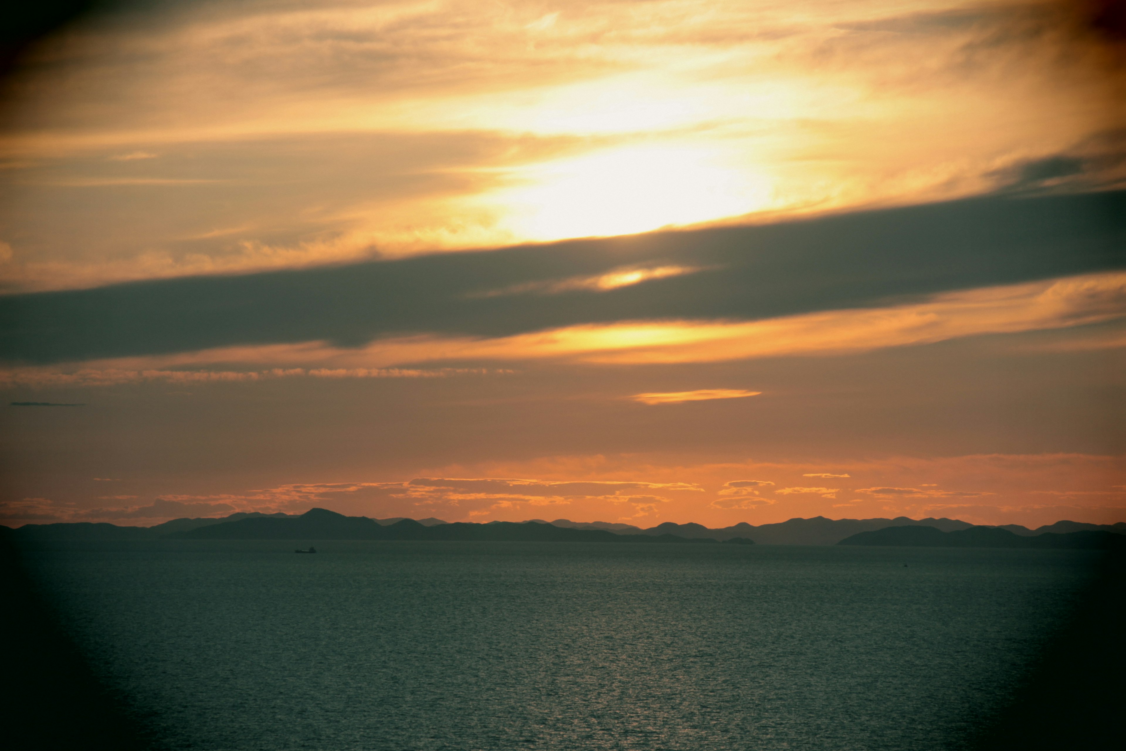 夕日が海に反射する風景　雲が広がり温かい色合い　静かな海面