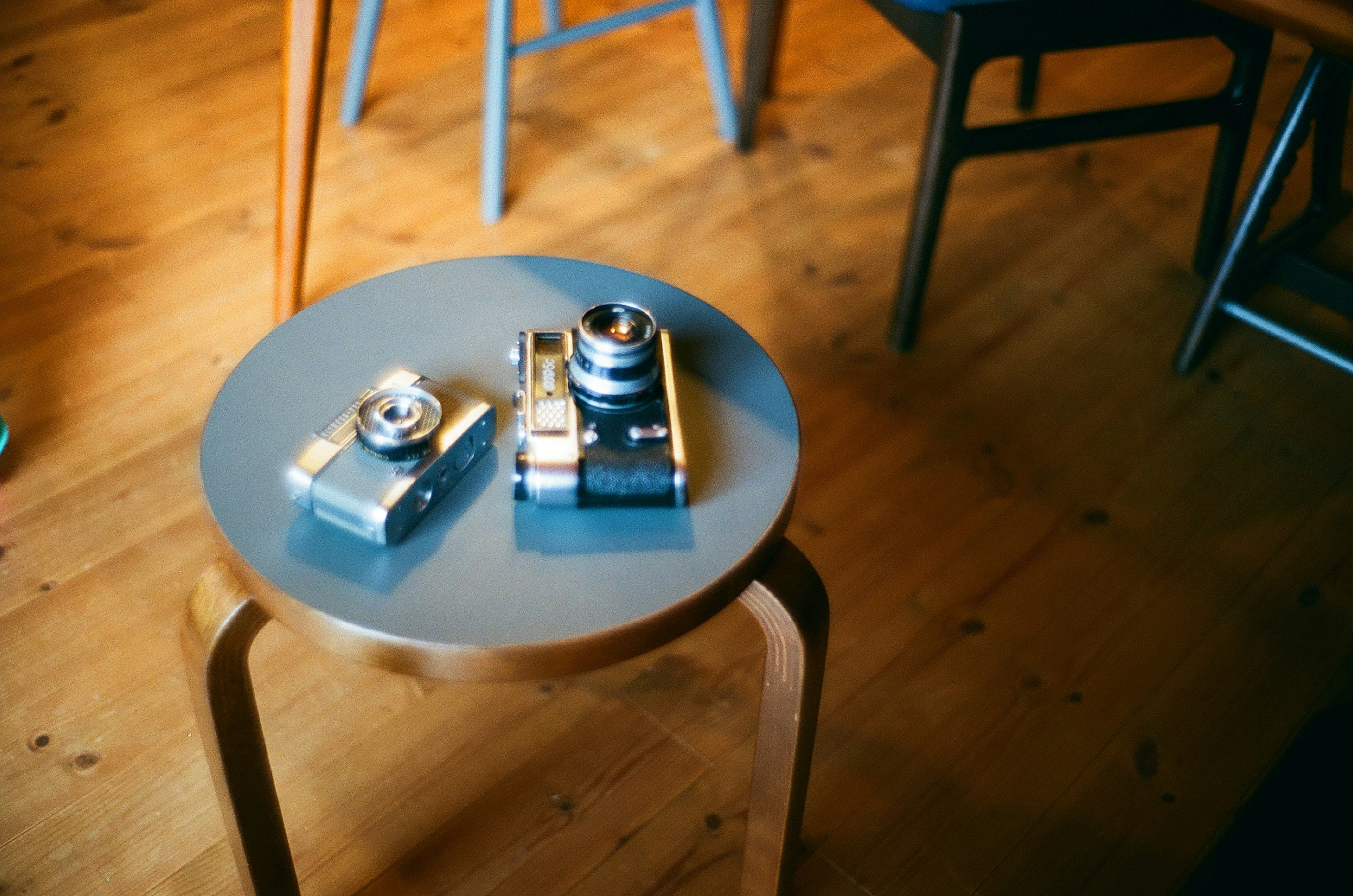 Two cameras on a round table with a wooden floor