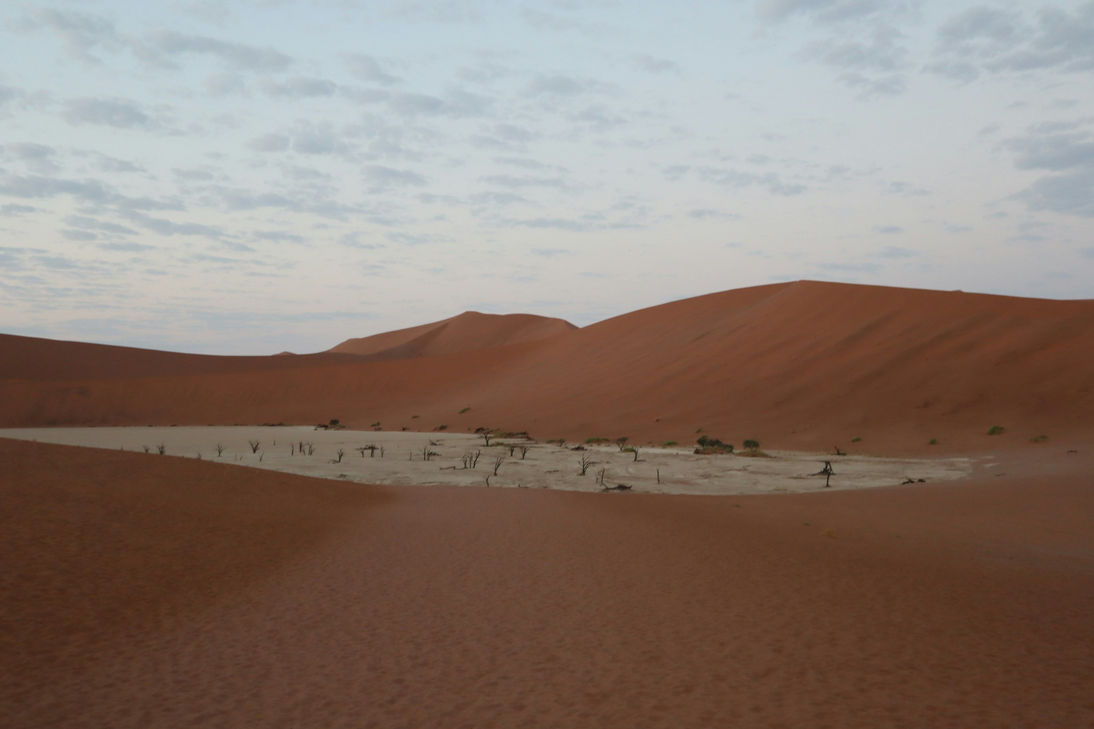 Vast sand dunes with a dry landscape under a cloudy sky