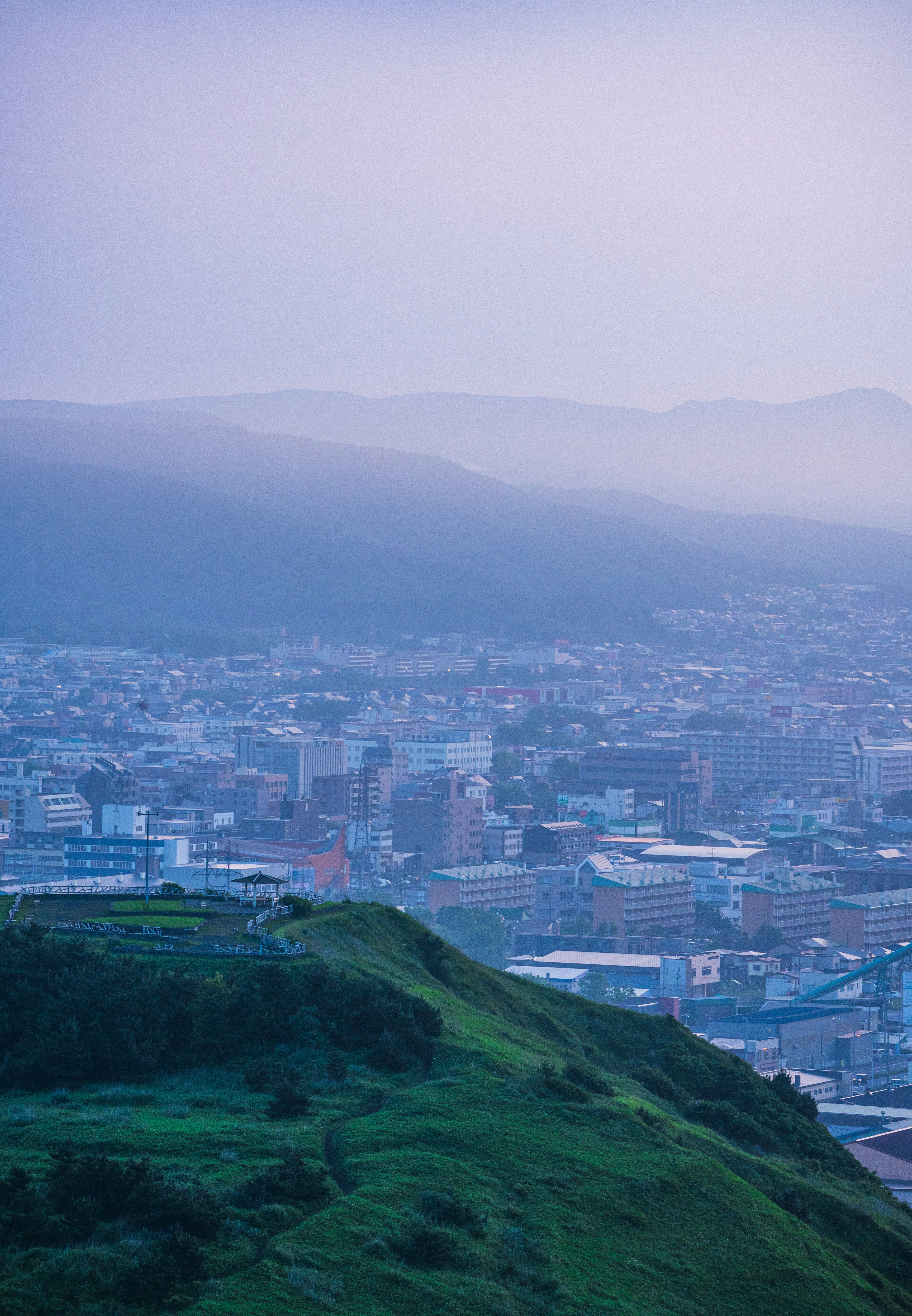 霧に包まれた都市の眺め 緑の丘と遠くの山々が見える