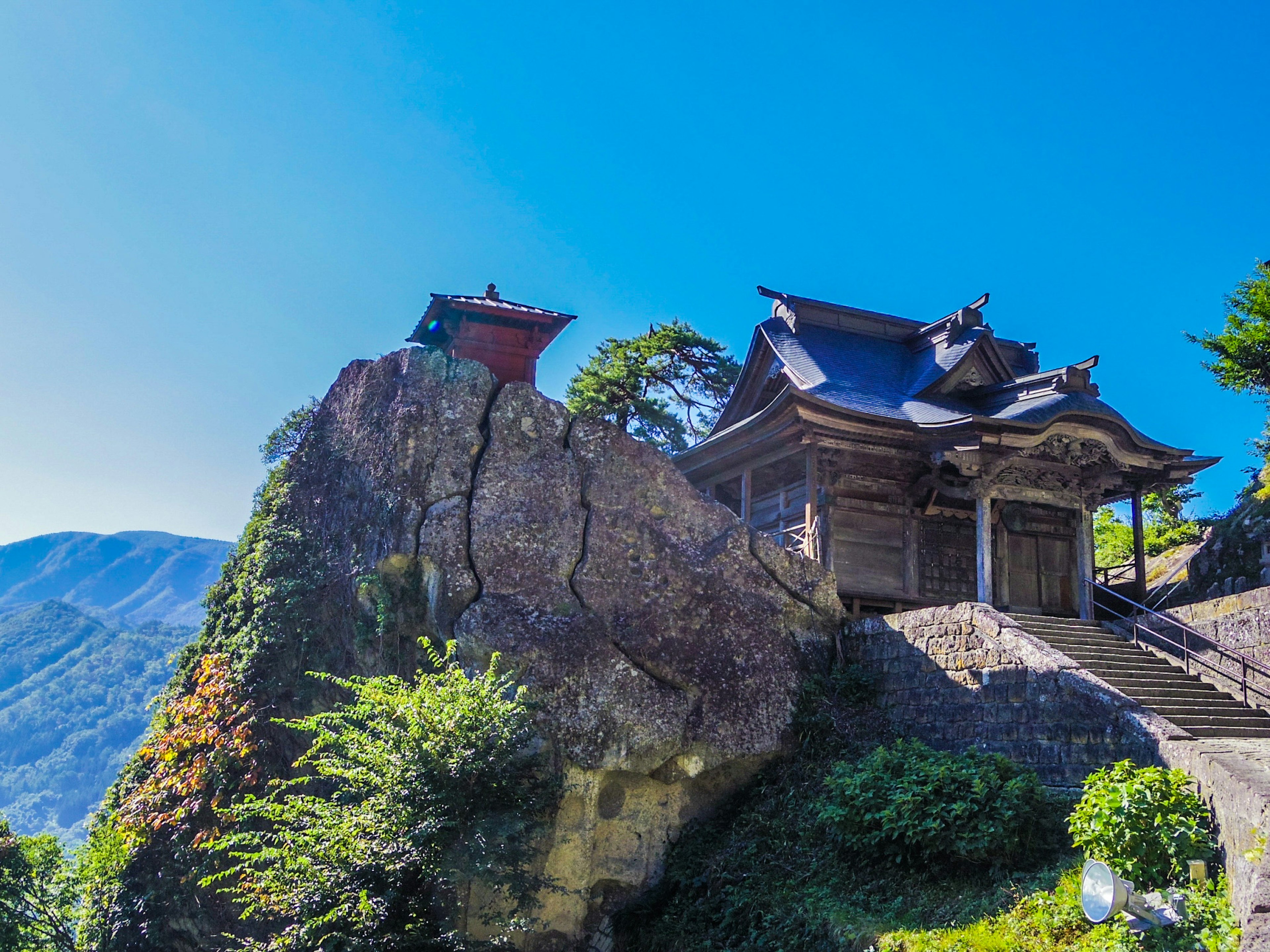 在蓝天下矗立于岩石上的古老神社，四周环绕着绿色植物