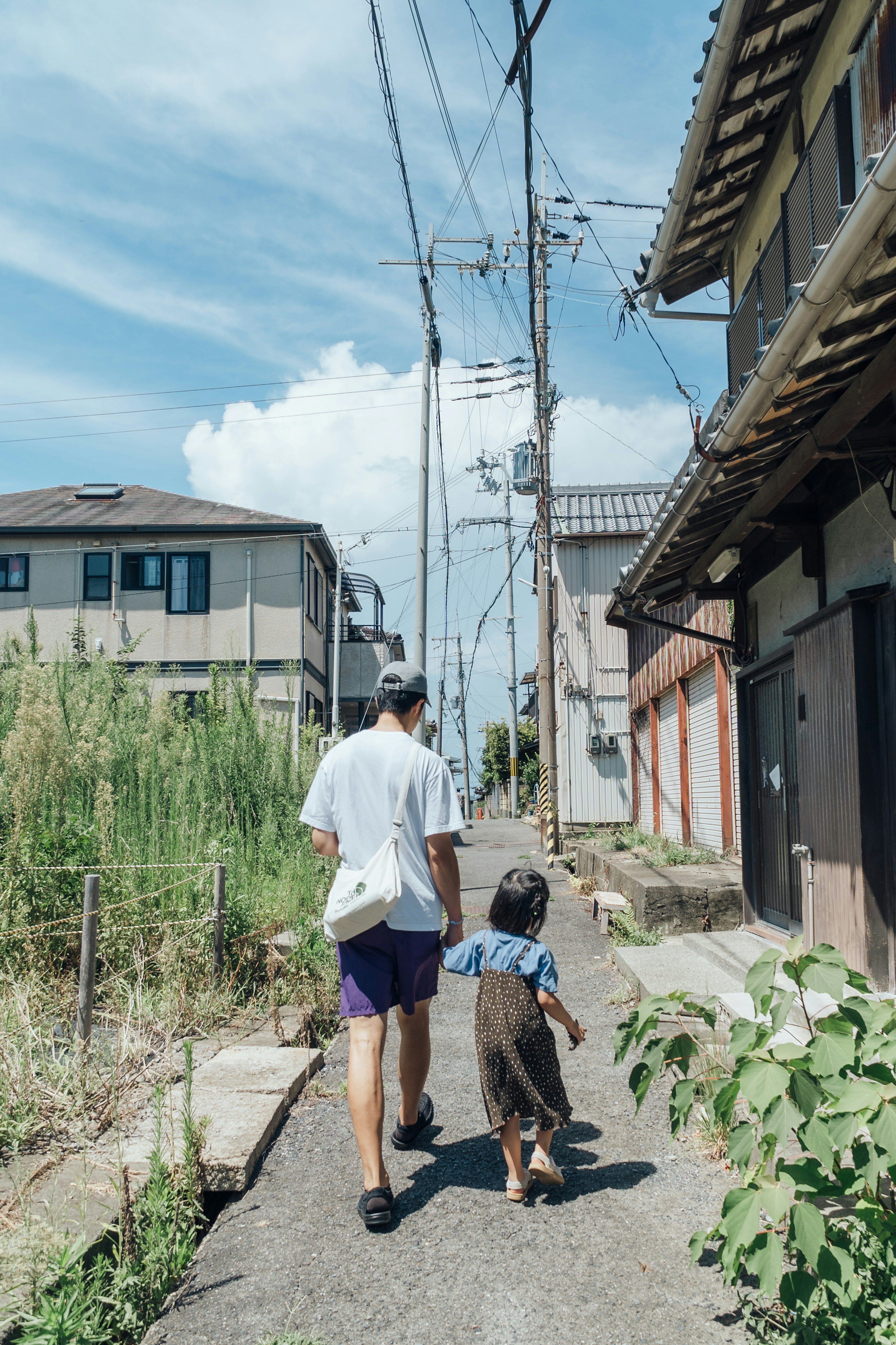 Un genitore e un bambino che camminano su un sentiero tranquillo con cielo azzurro e nuvole