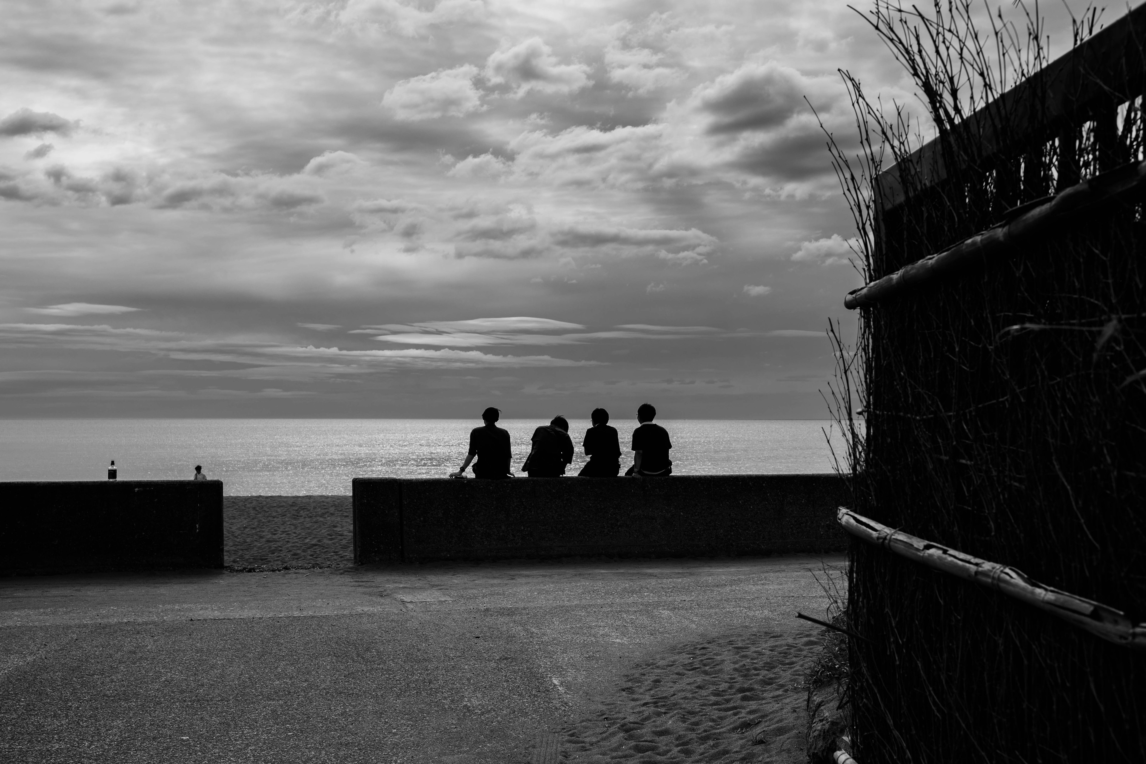 Silhouetten von vier Personen, die auf das Meer schauen, mit einem bewölkten Himmel