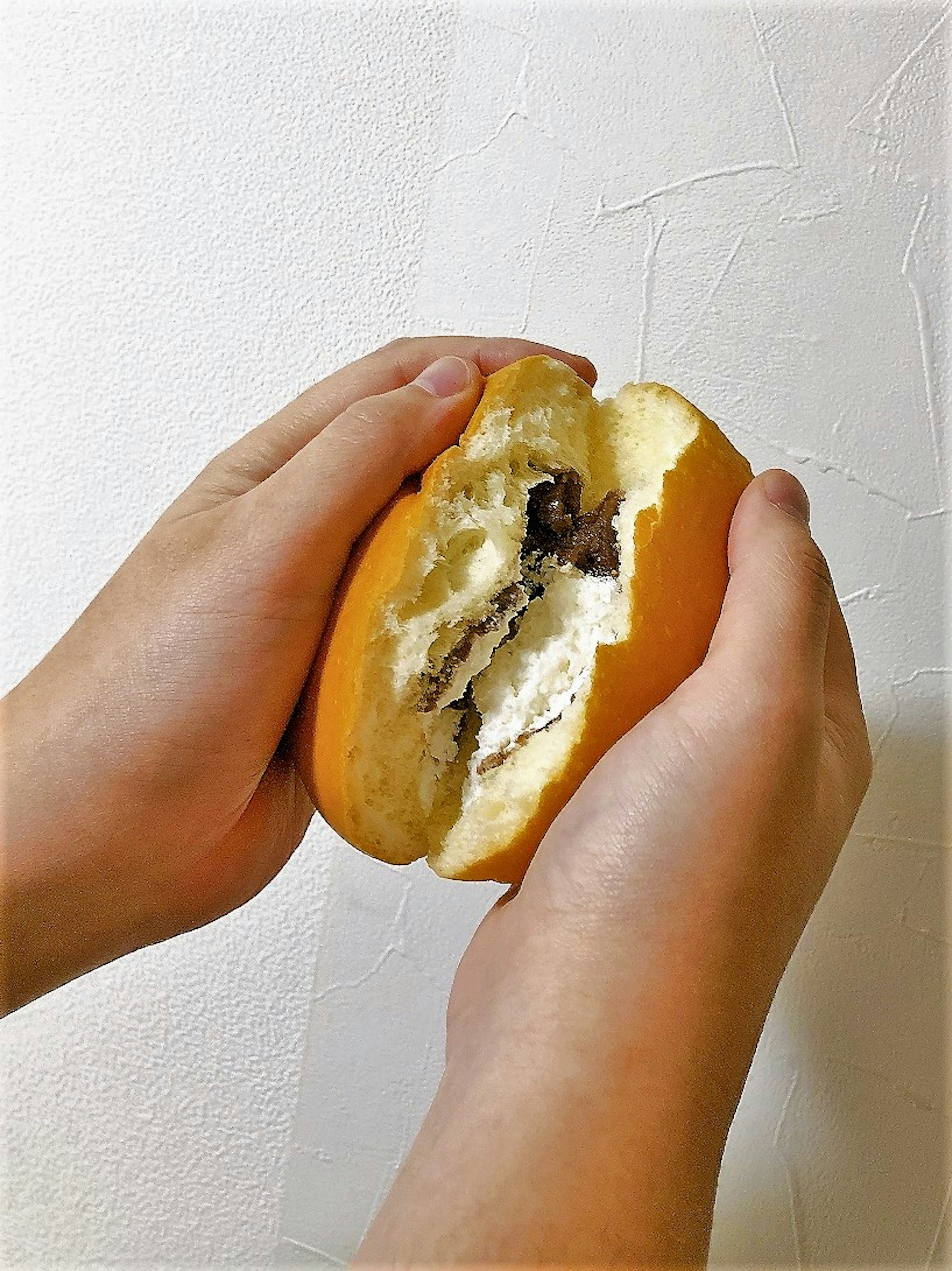 A cream-filled bun being split in half held by hands