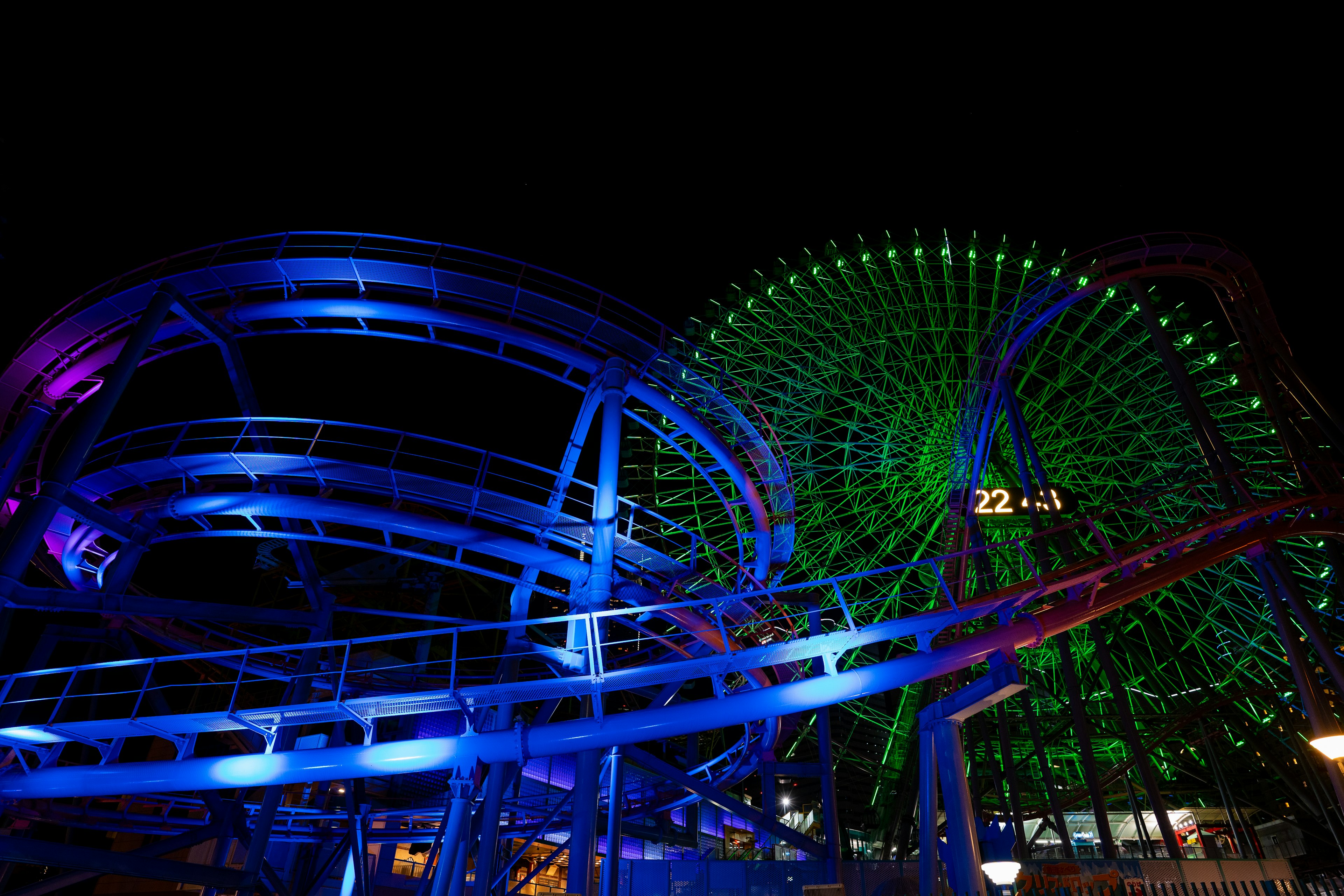 Rueda de la fortuna y montaña rusa iluminadas por la noche con luces azules y verdes