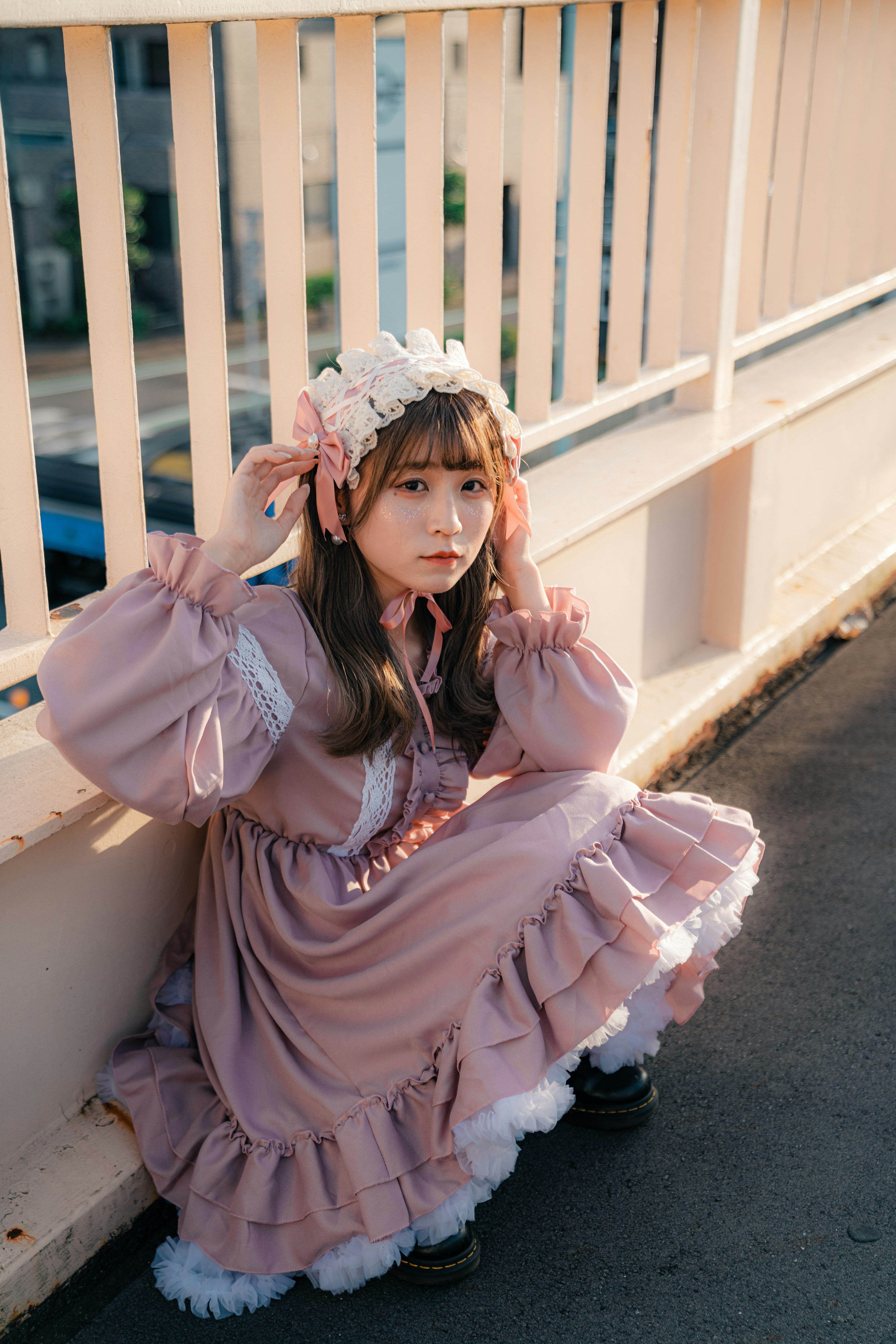 A girl in a pink dress with frills and ribbons sitting against a railing