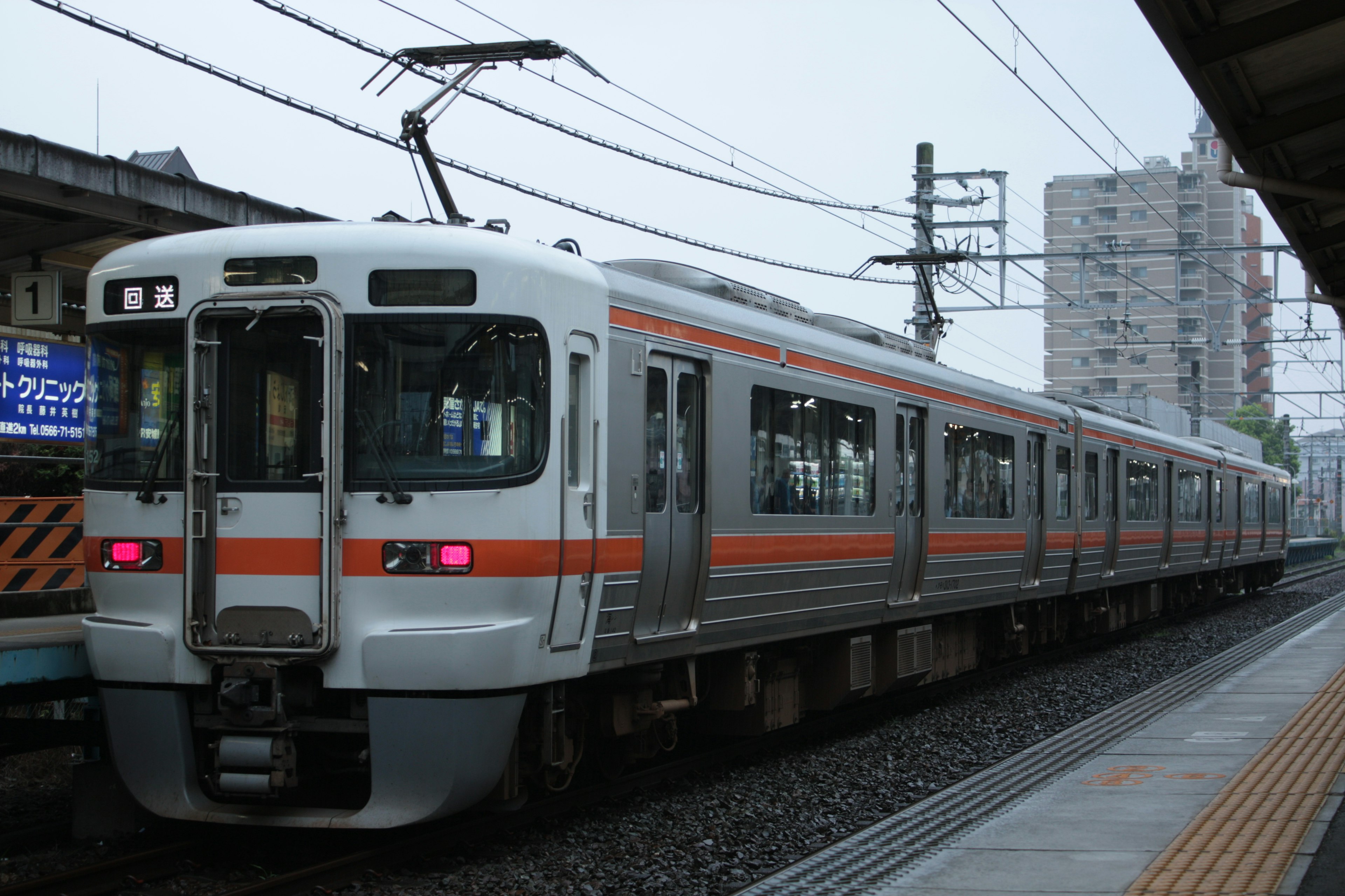 A Japanese commuter train with distinctive orange stripes is stopped at a station