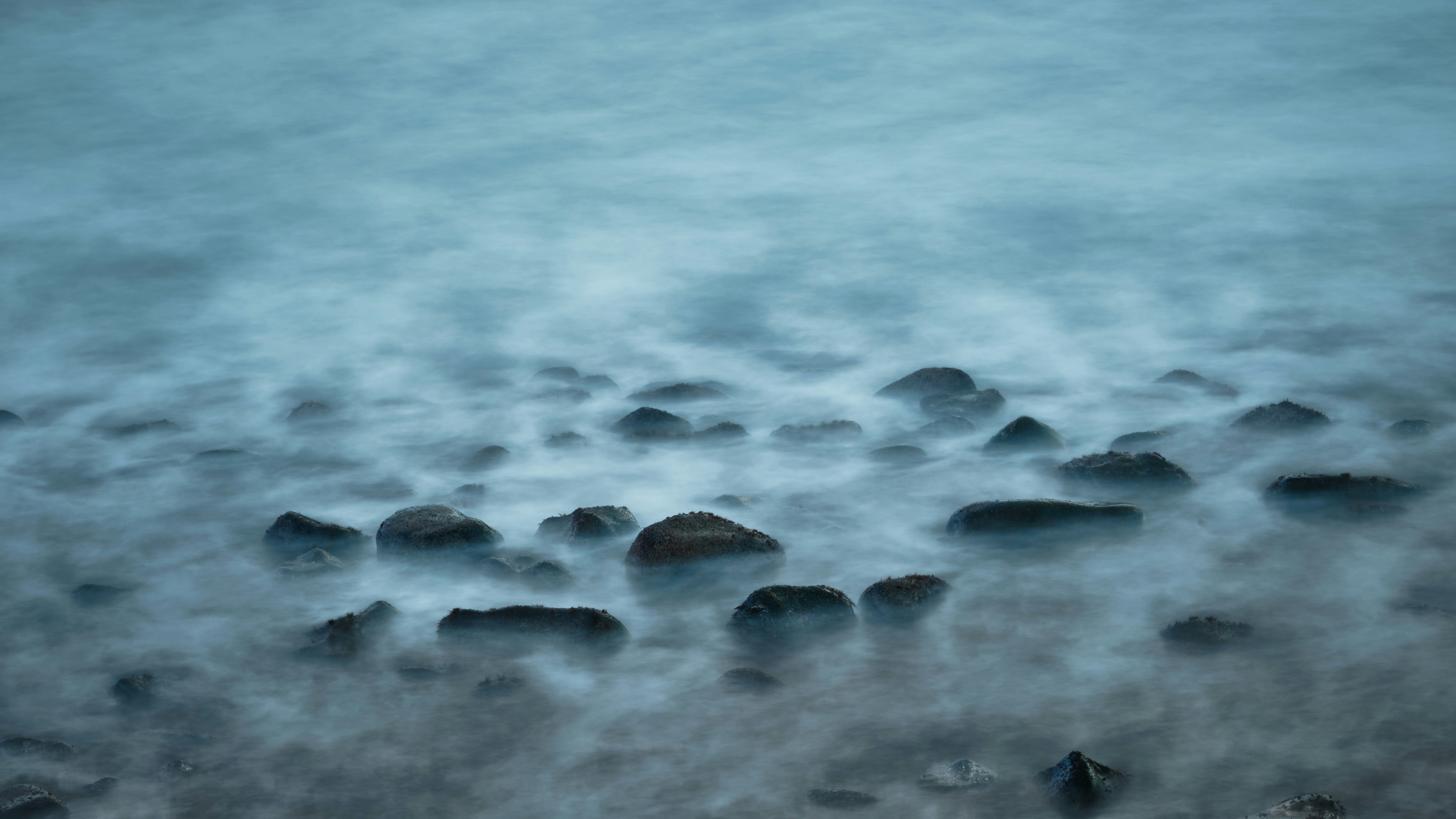 A photo of smooth water with visible stones beneath the surface in a blue hue