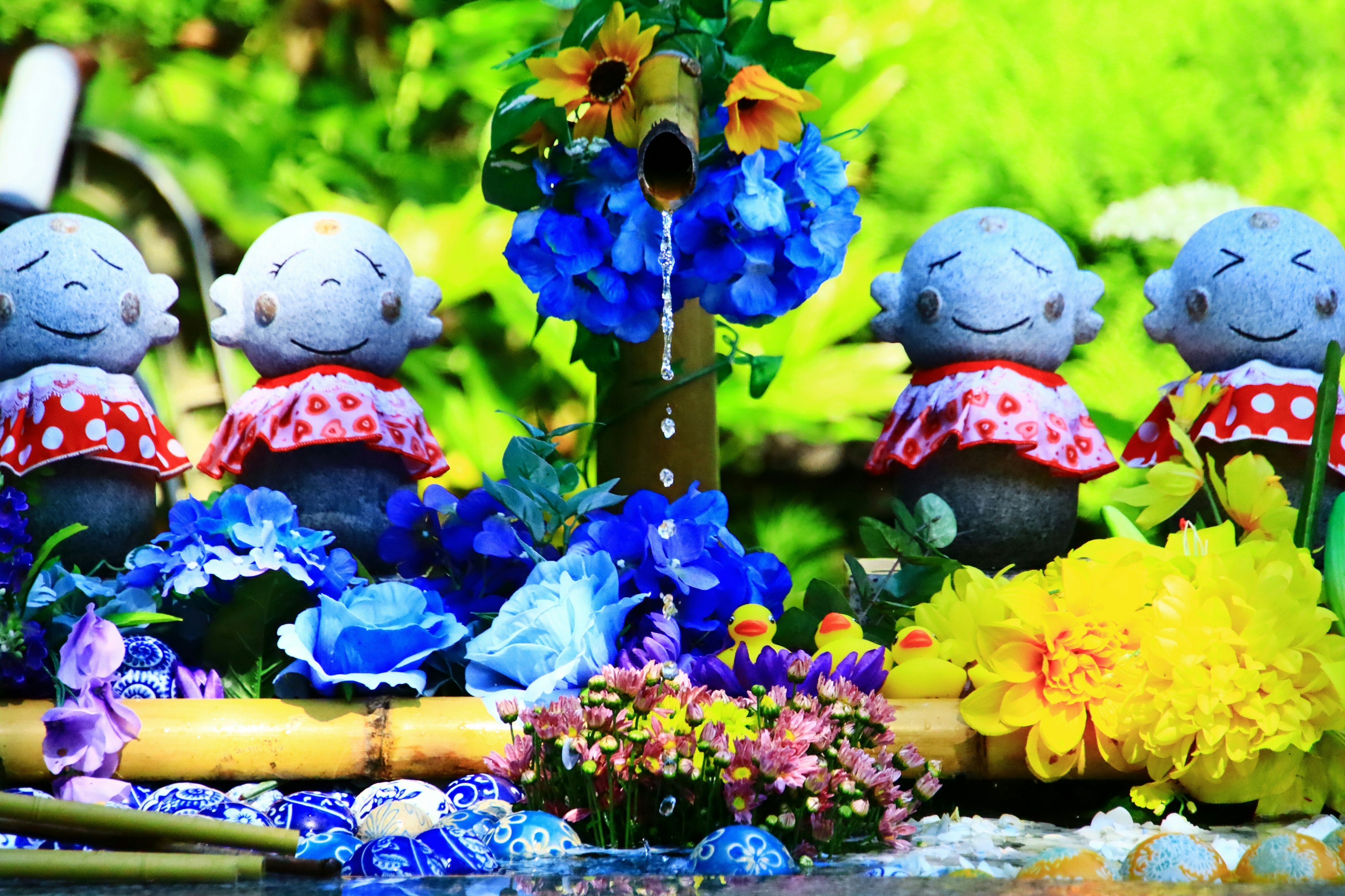 Colorful flowers and a water fountain with smiling ceramic figures nearby