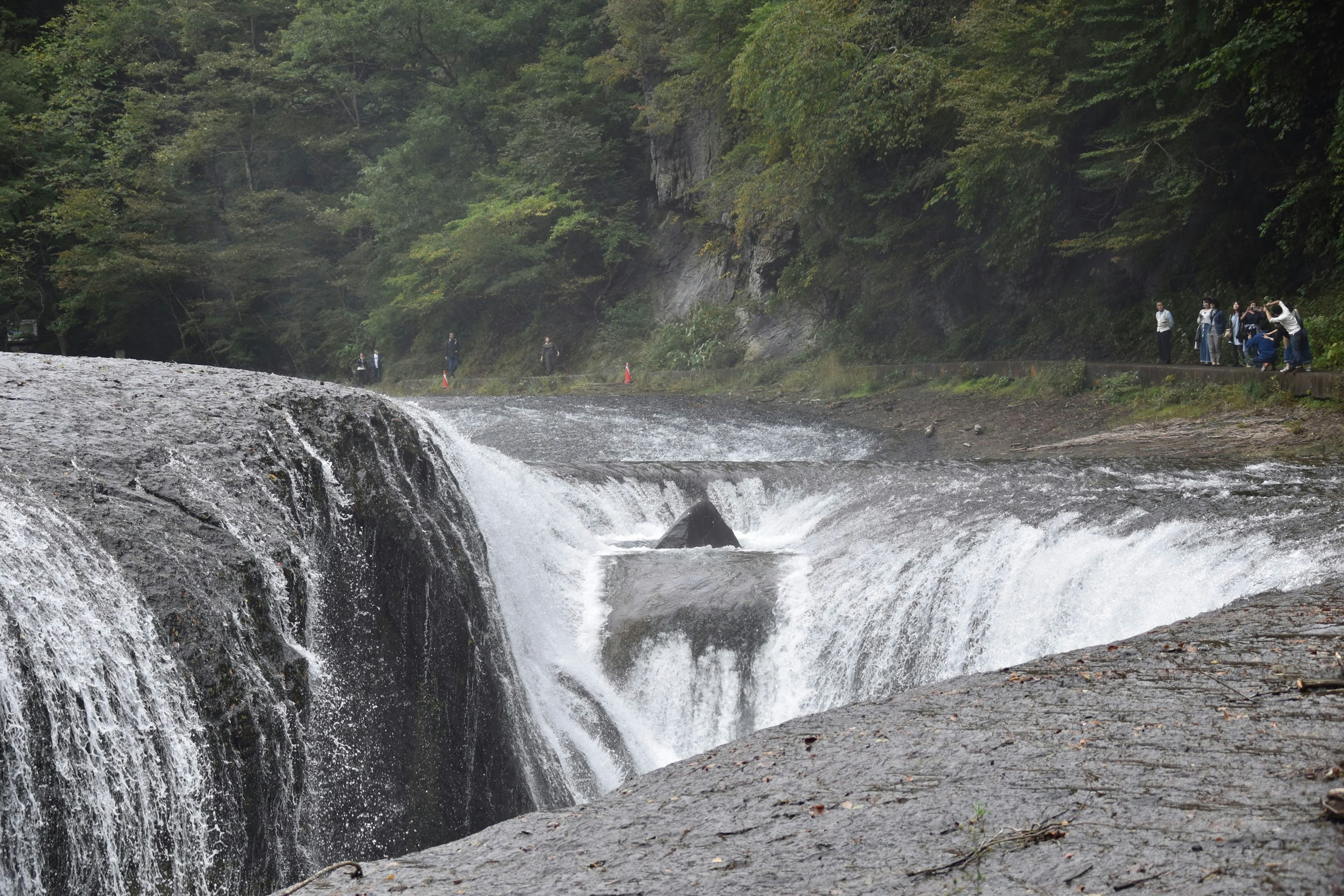 Una hermosa escena de una cascada que cae sobre rocas rodeadas de exuberante vegetación y personas