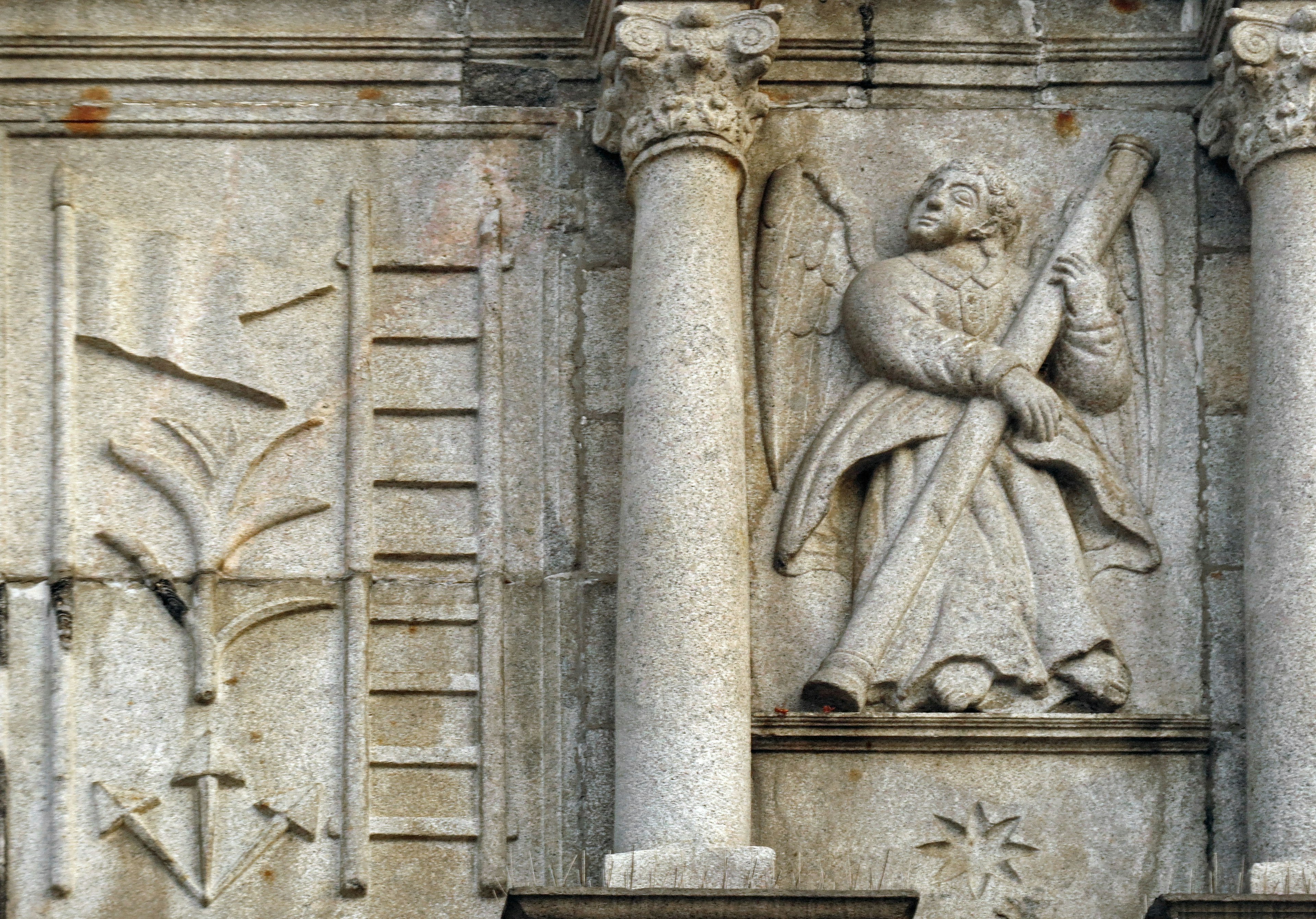 Scultura di angelo con un bastone su un muro di pietra con motivi vegetali