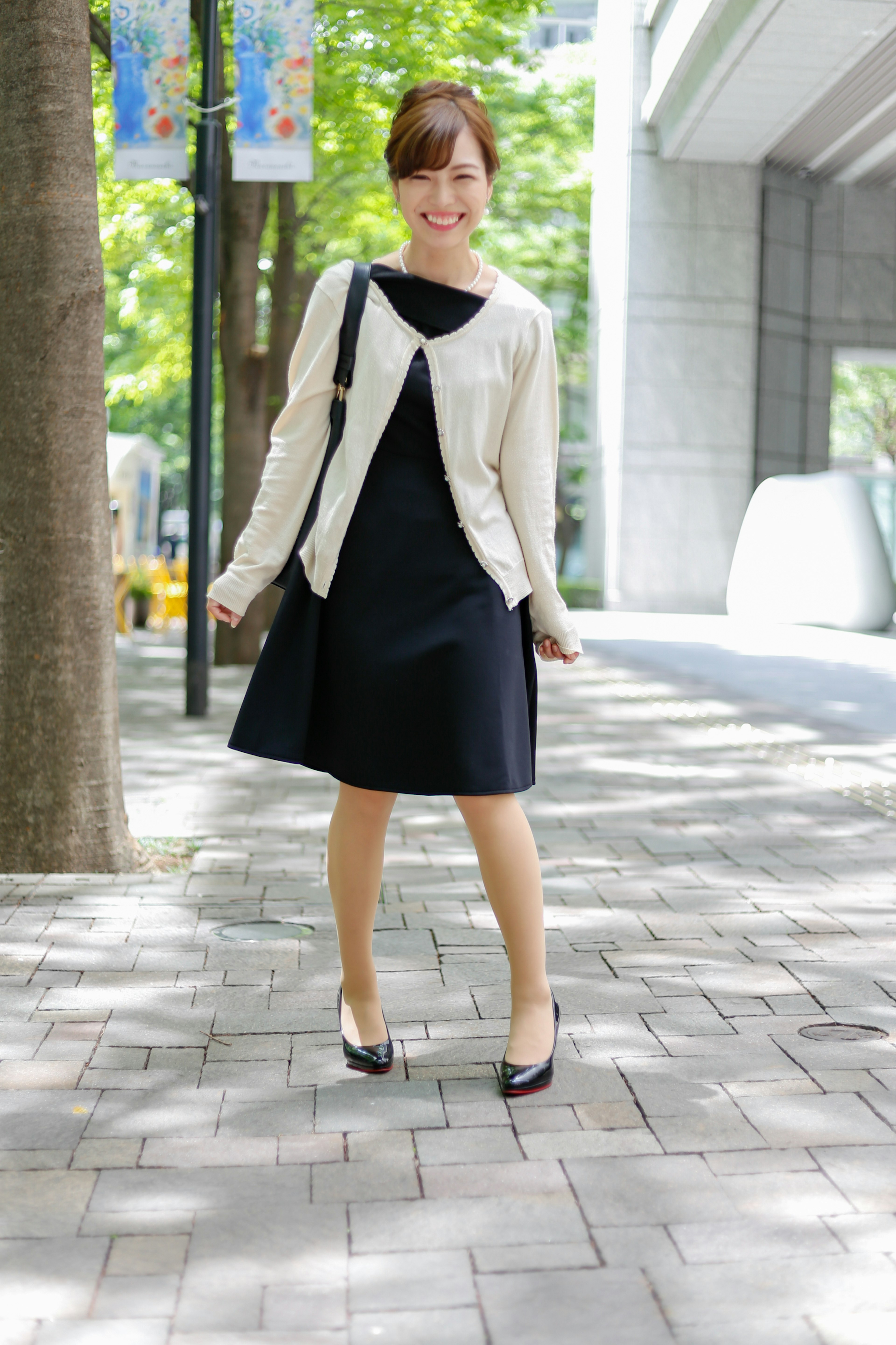 Woman in white cardigan and black dress standing on a city sidewalk