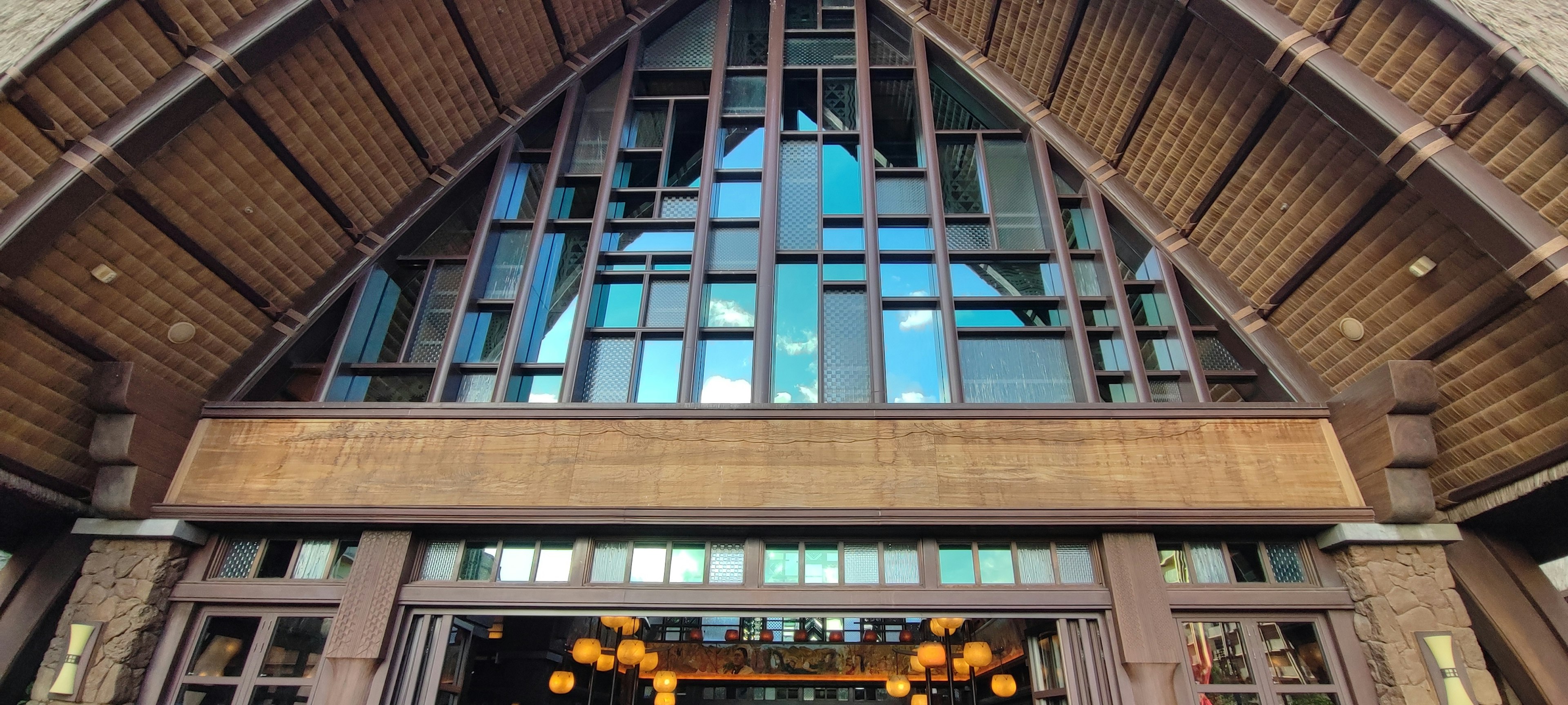 Entrée d'un bâtiment avec un toit triangulaire en bois grandes fenêtres en verre et éclairage chaleureux