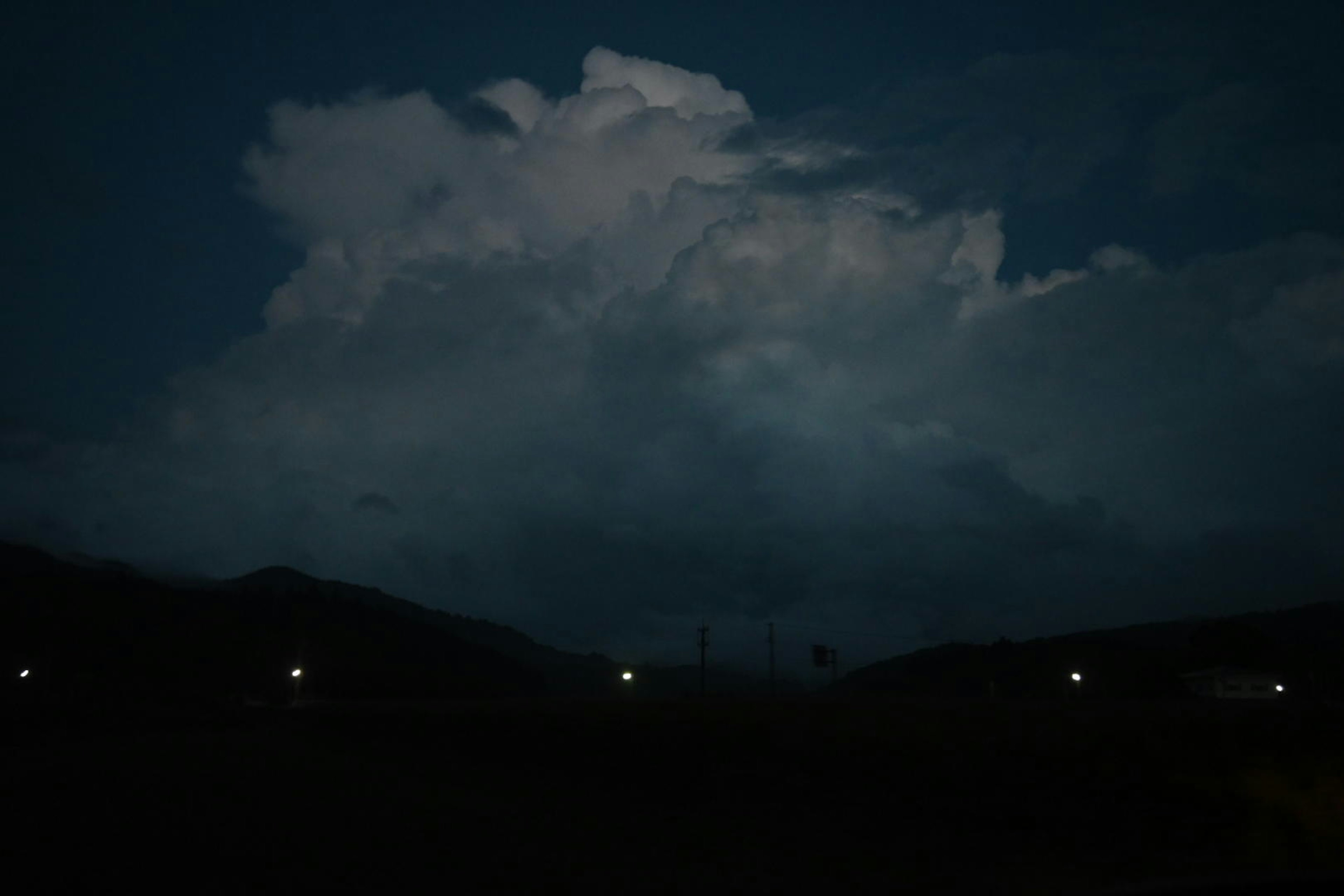 Grands nuages illuminés contre un ciel nocturne sombre avec des silhouettes de montagnes au loin