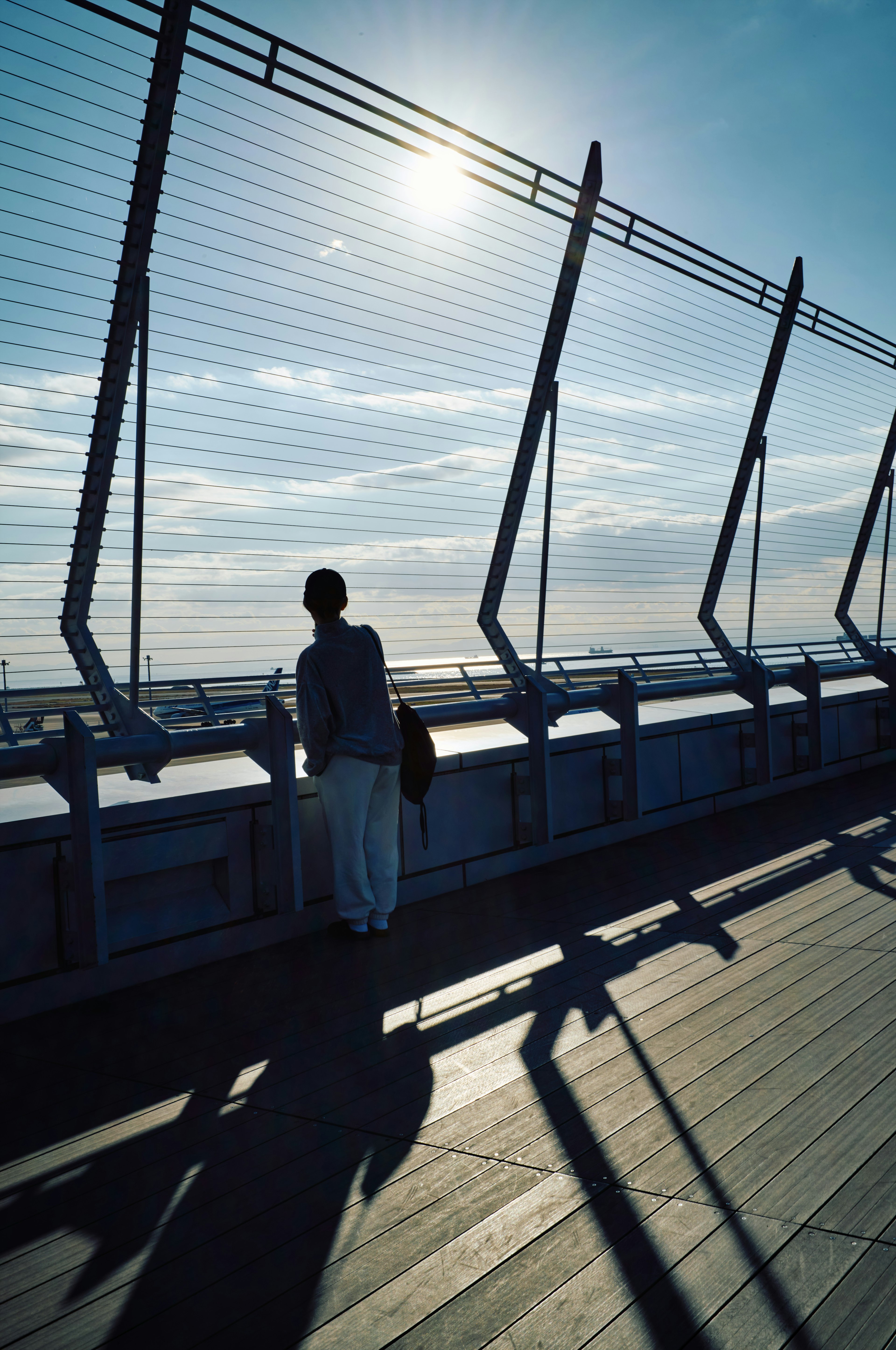 Silhouette di una persona appoggiata a un parapetto sotto un cielo blu