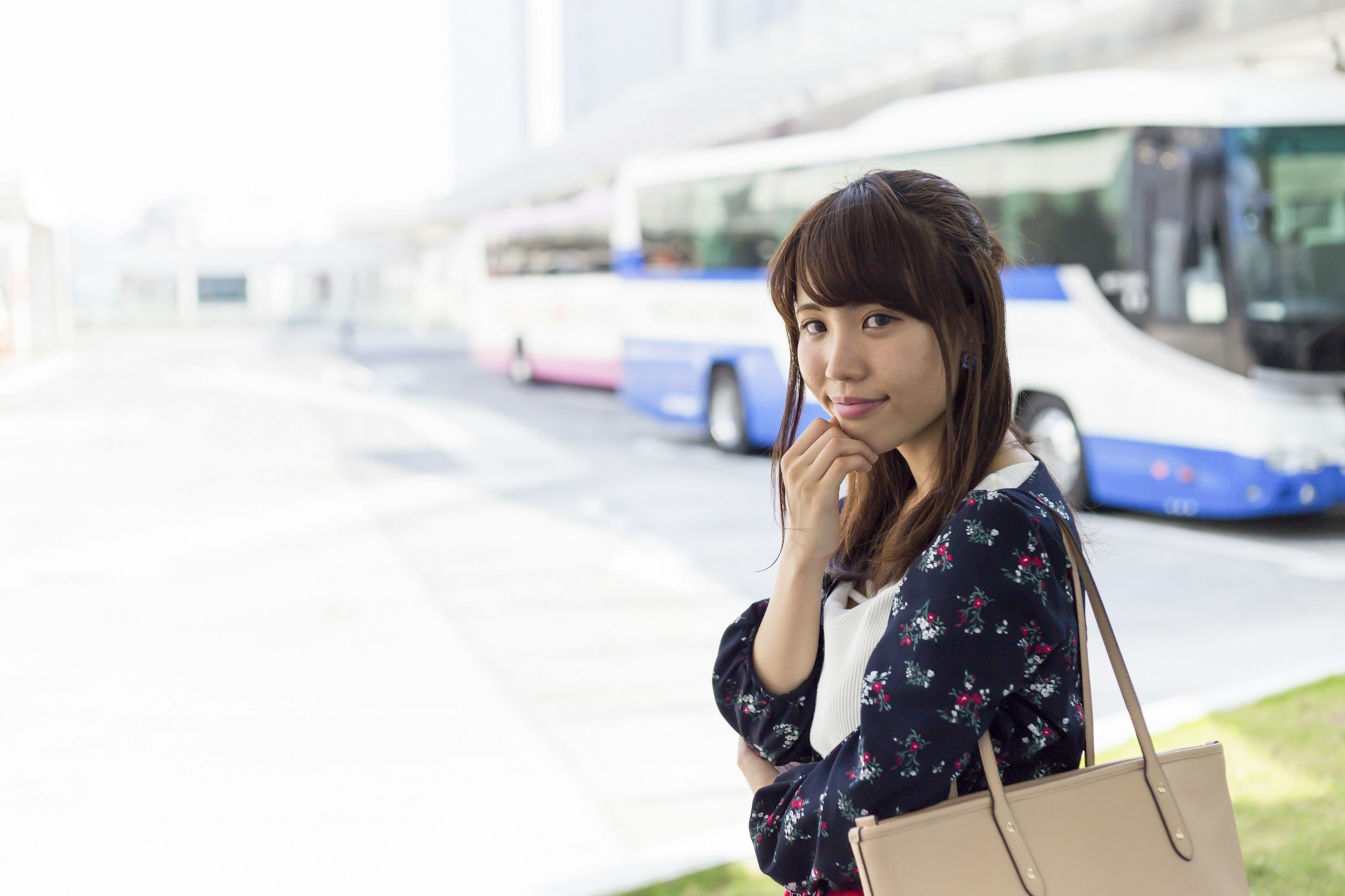 A woman pondering at a bus stop with buses parked in the background