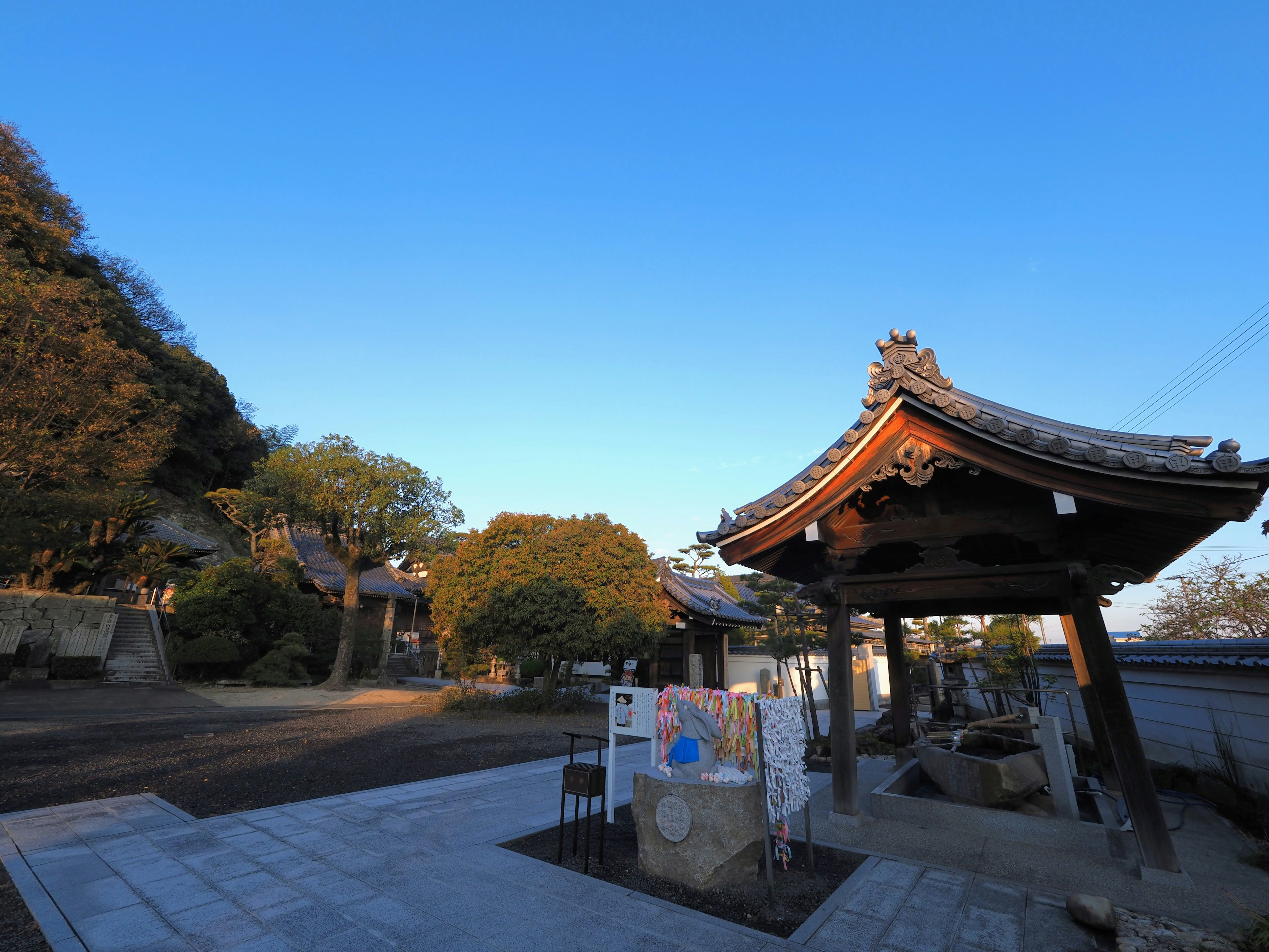 Torre de campanas de un templo japonés tradicional bajo un cielo azul claro con vegetación circundante