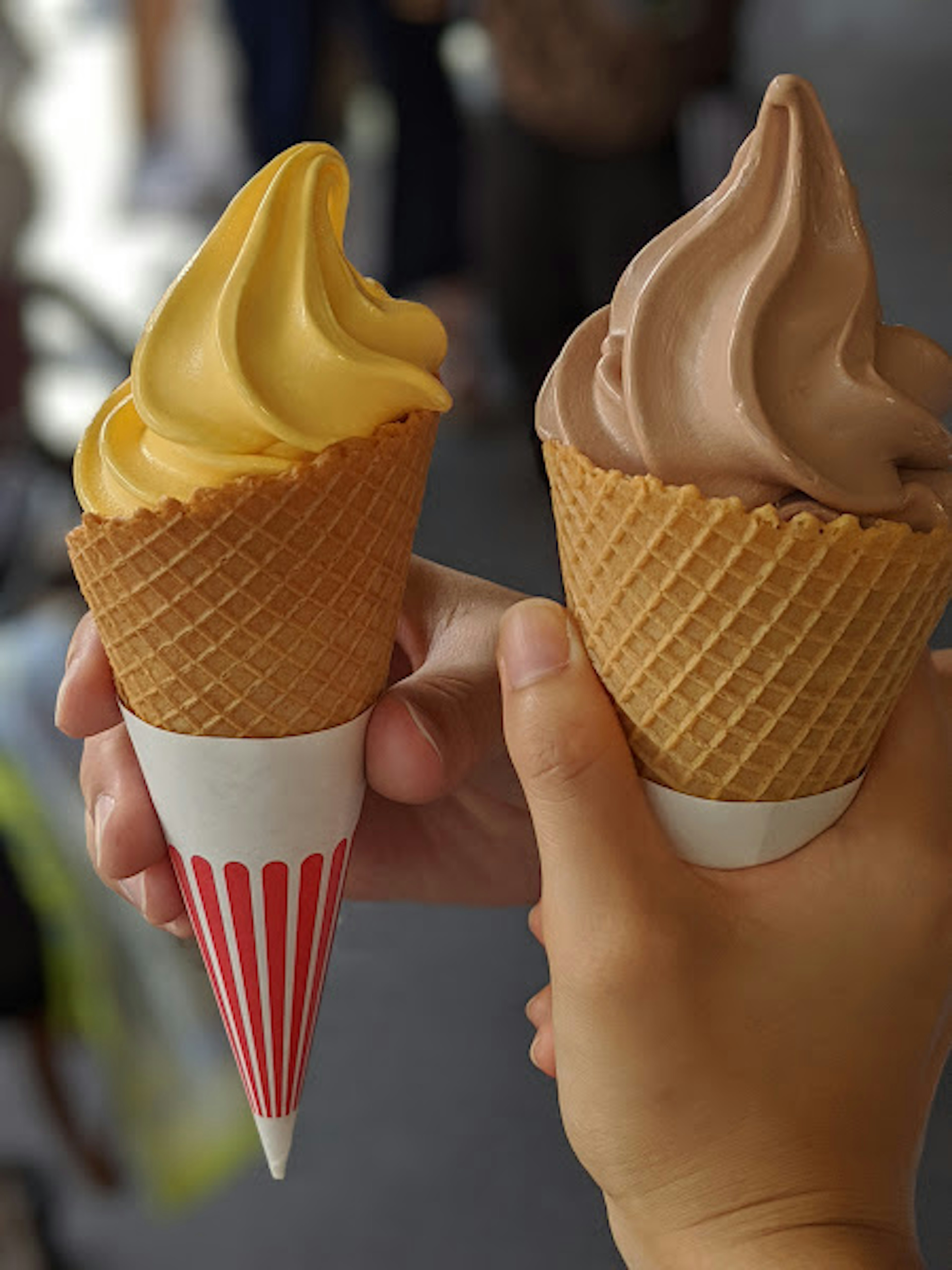 Dos conos de helado en mano uno de vainilla y uno de chocolate