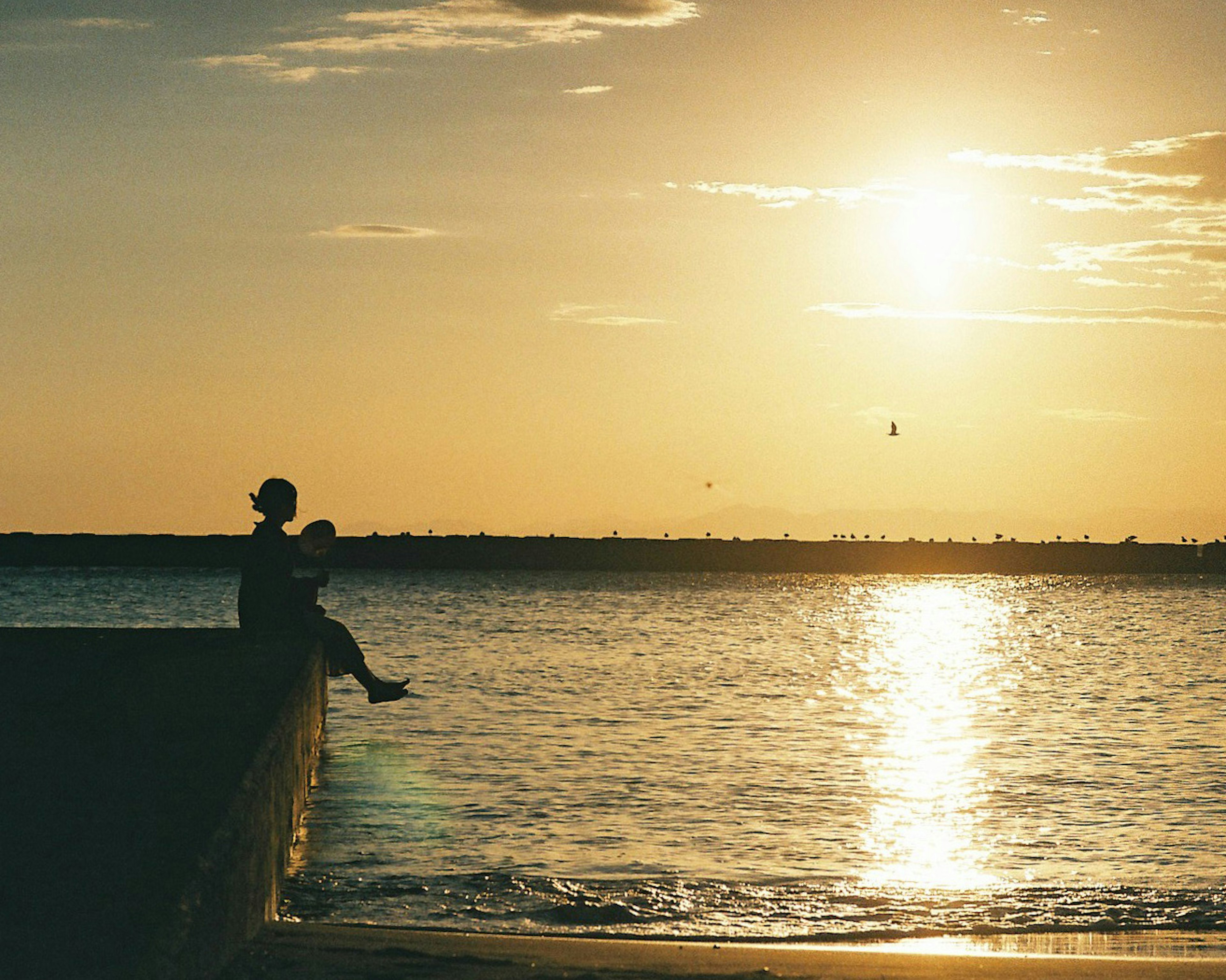 Silhouette eines Elternteils und eines Kindes, die am Meer im Sonnenuntergang sitzen