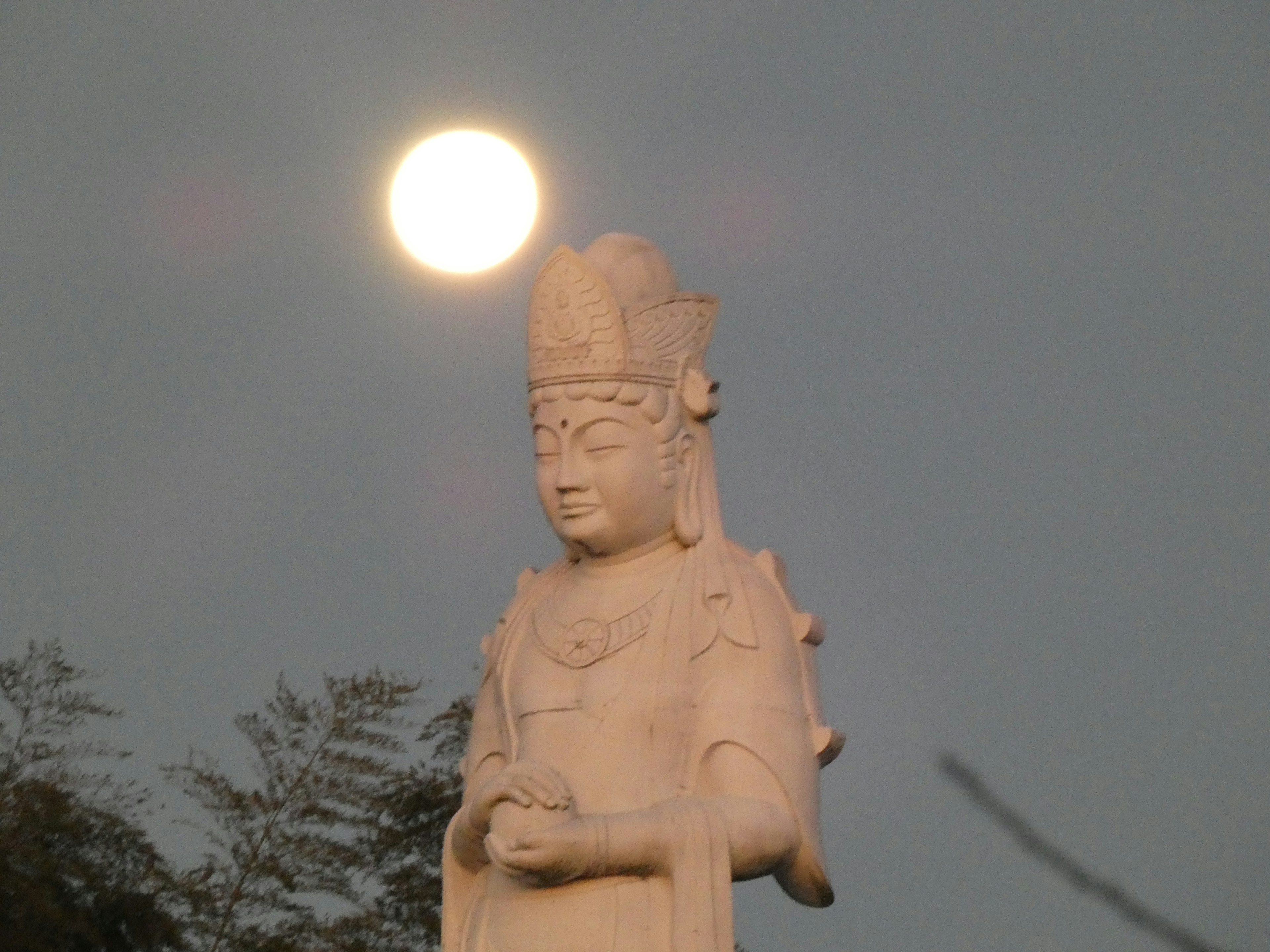 Statua bianca che si erge contro una grande luna sullo sfondo